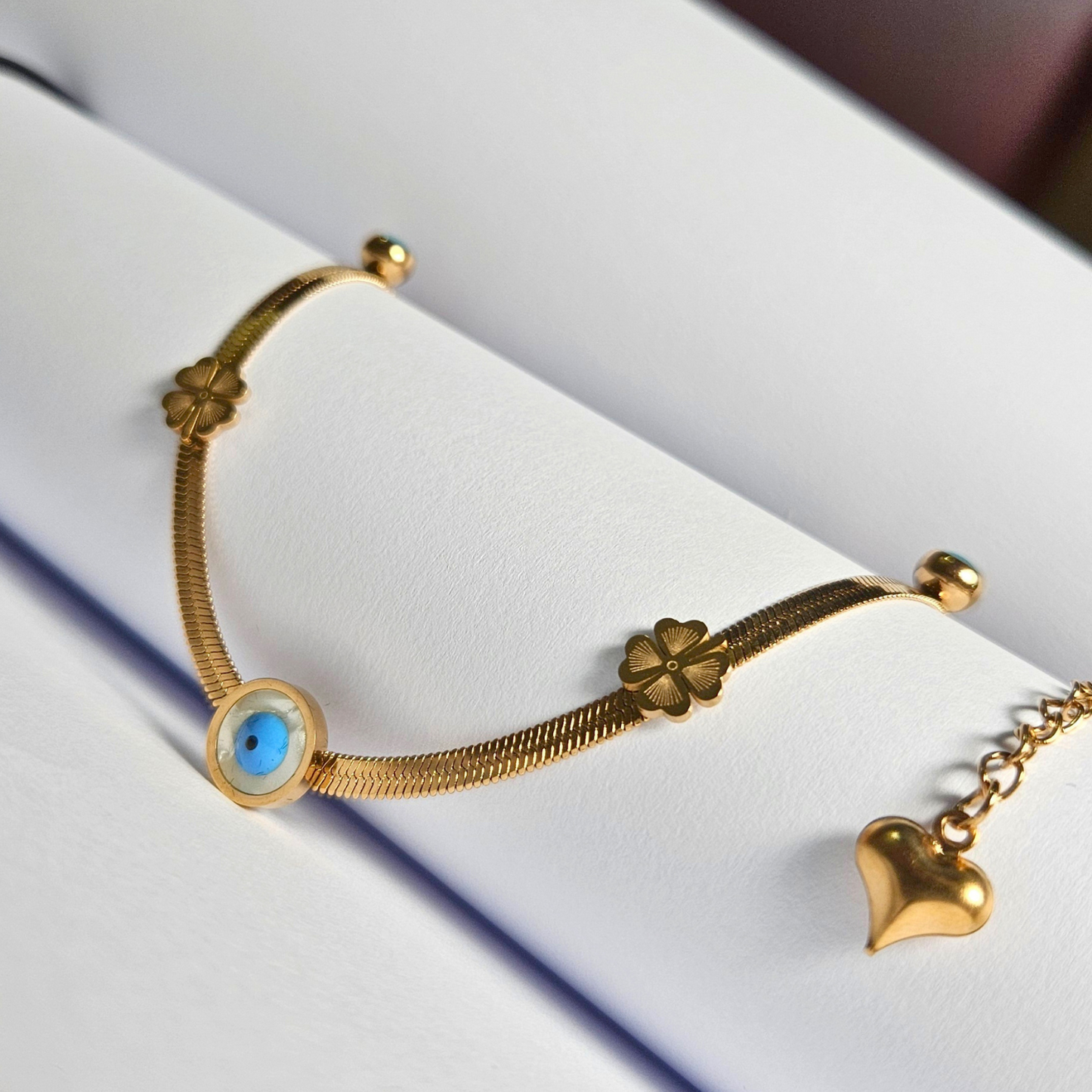 Gold bracelet with clover and heart charm on a white surface