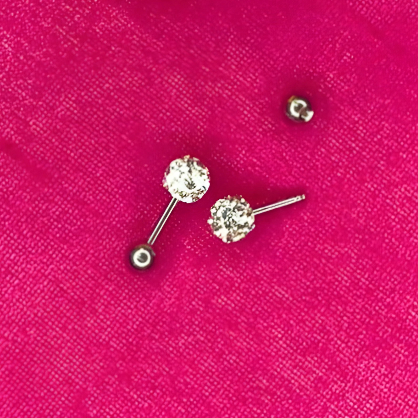 Silver ball earrings with clear gemstones on a pink background
