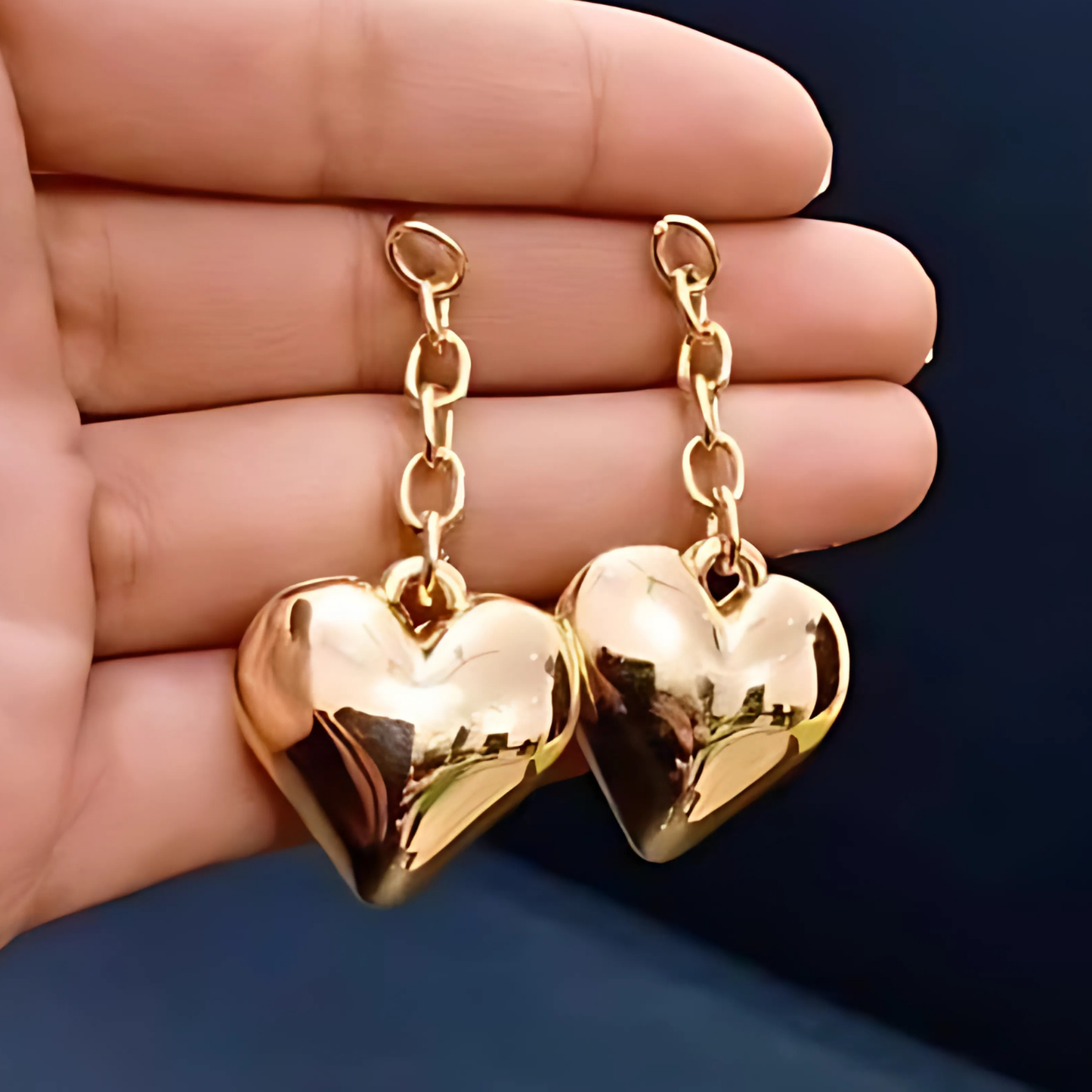 Gold heart-shaped earrings held between fingers against a dark background