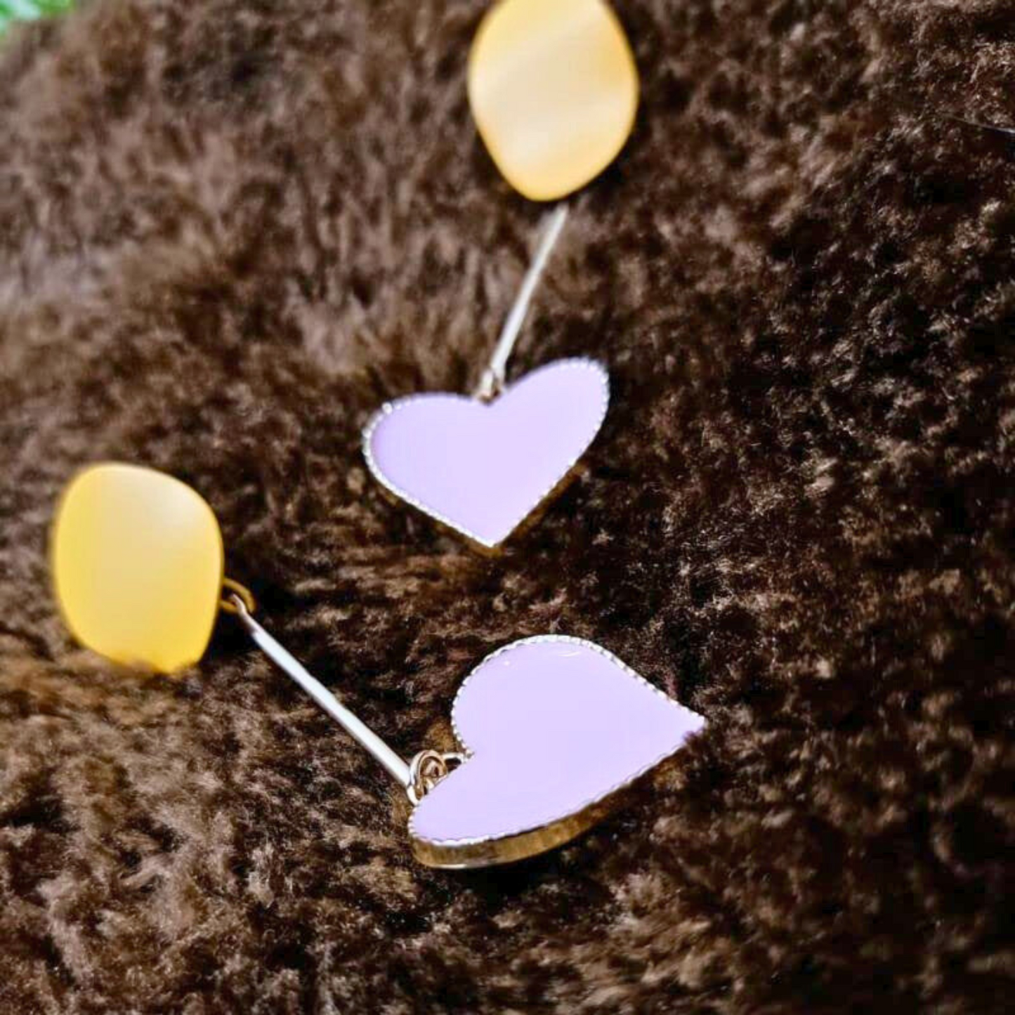 Heart-shaped earrings with yellow and pink hearts on a brown textured background