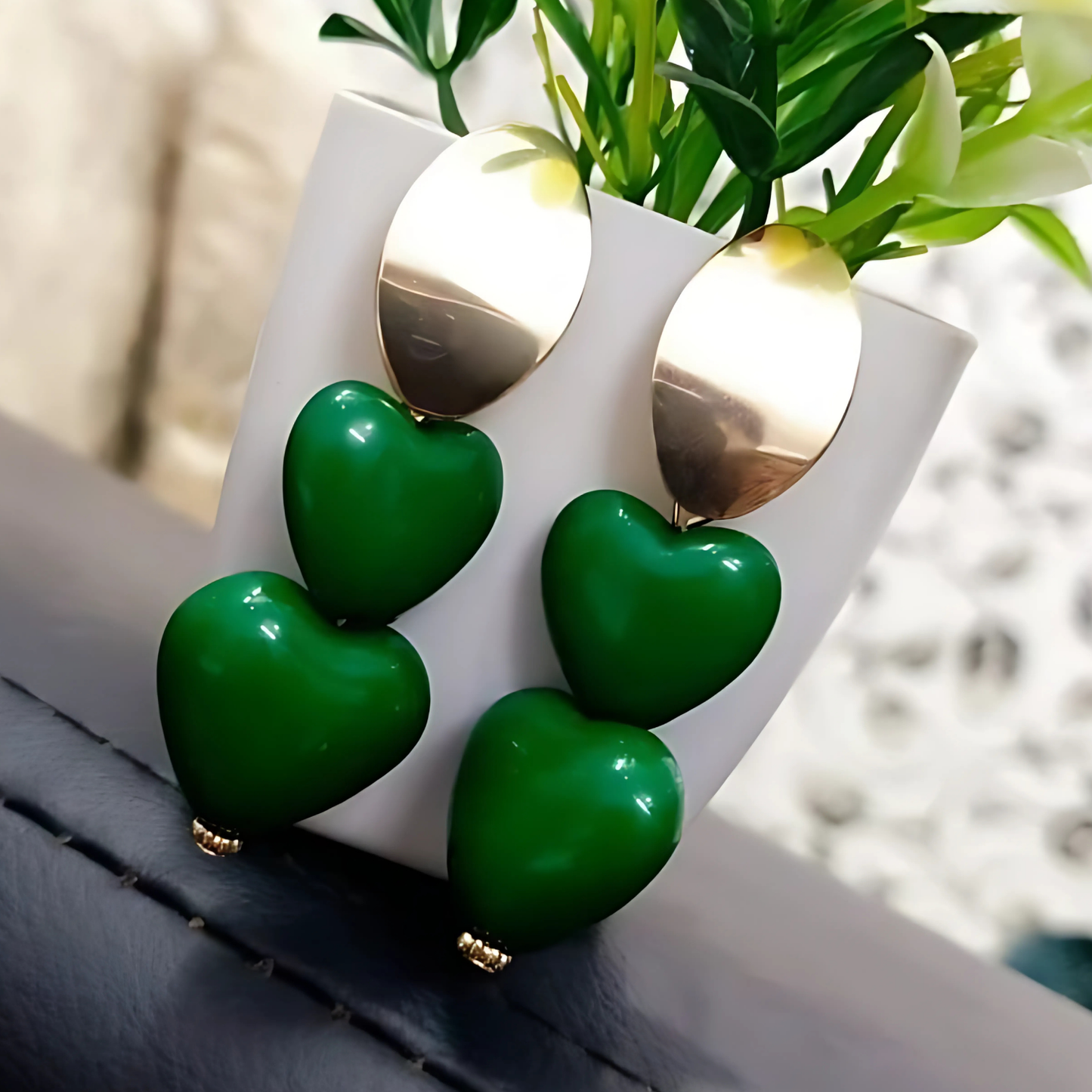 Green heart-shaped earrings on a white stand with a blurred background