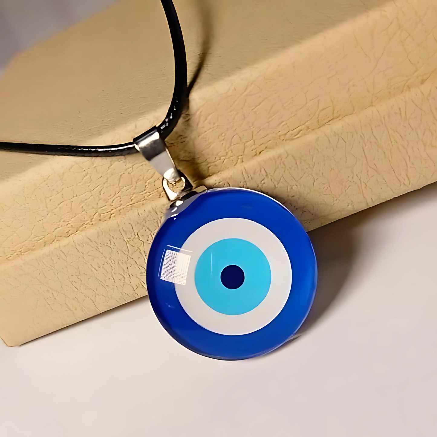 Blue and white evil eye pendant on a black cord against a beige background