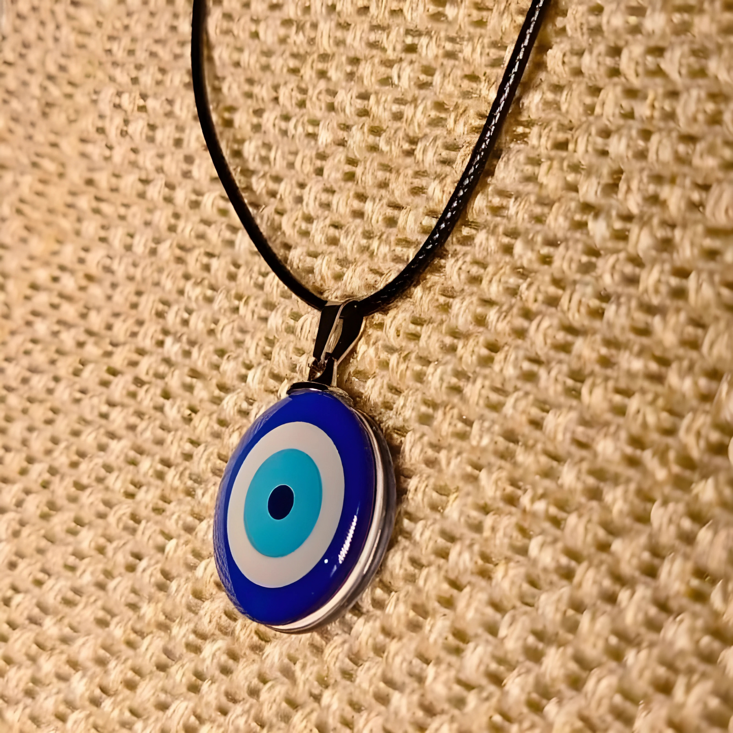 Blue and white evil eye pendant on a black cord against a beige woven background
