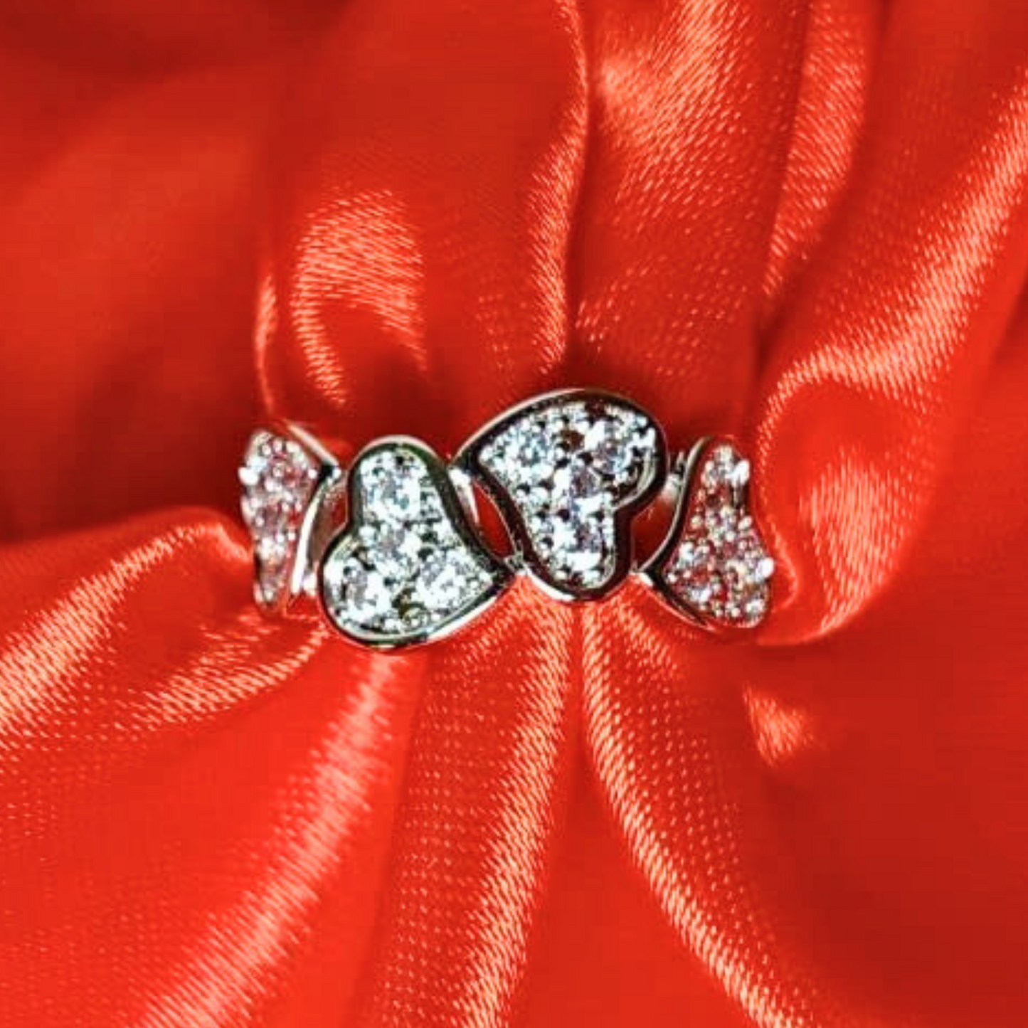 Silver ring with heart-shaped gemstones on a red satin background