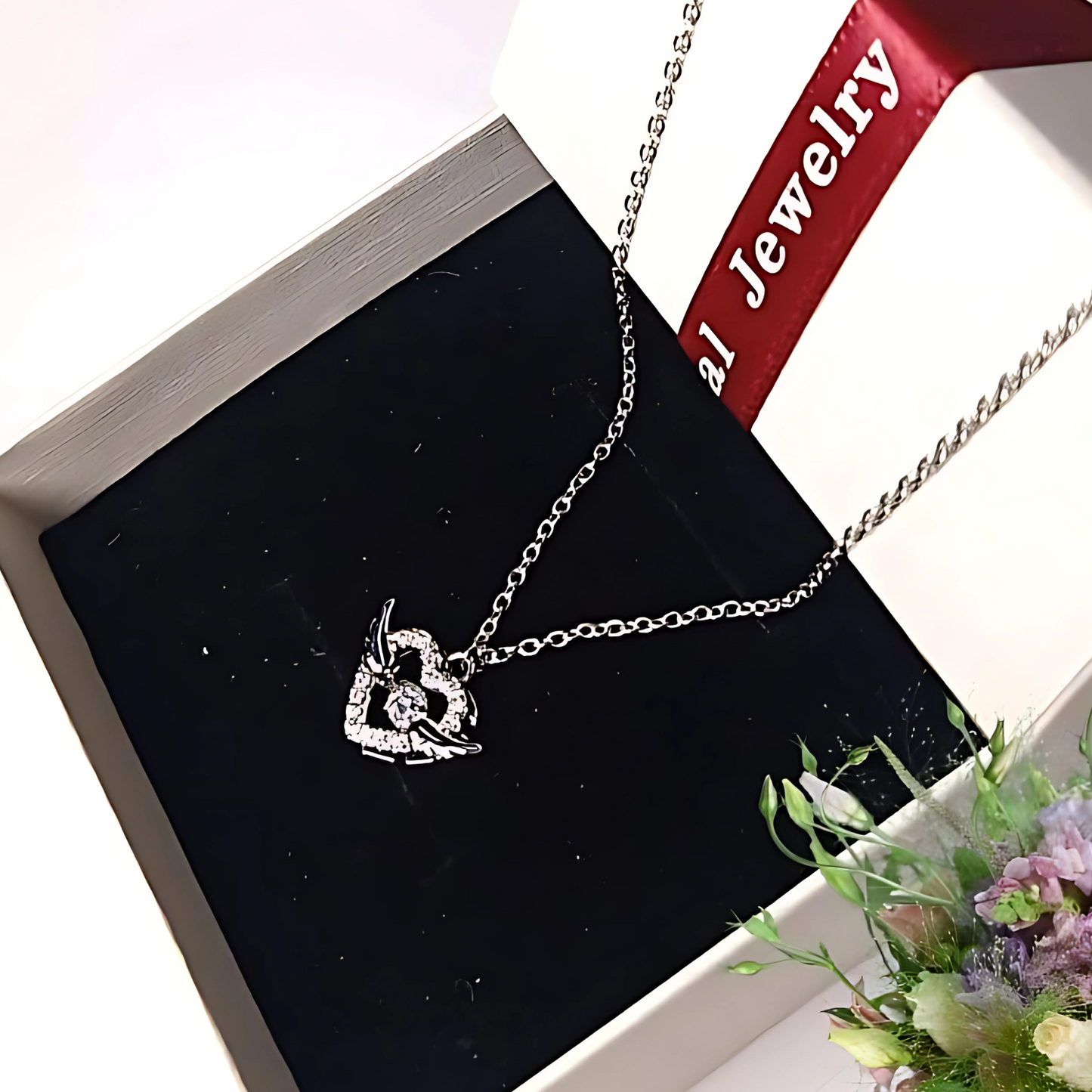 Silver necklace with a heart-shaped pendant on a black jewelry box with a red ribbon.