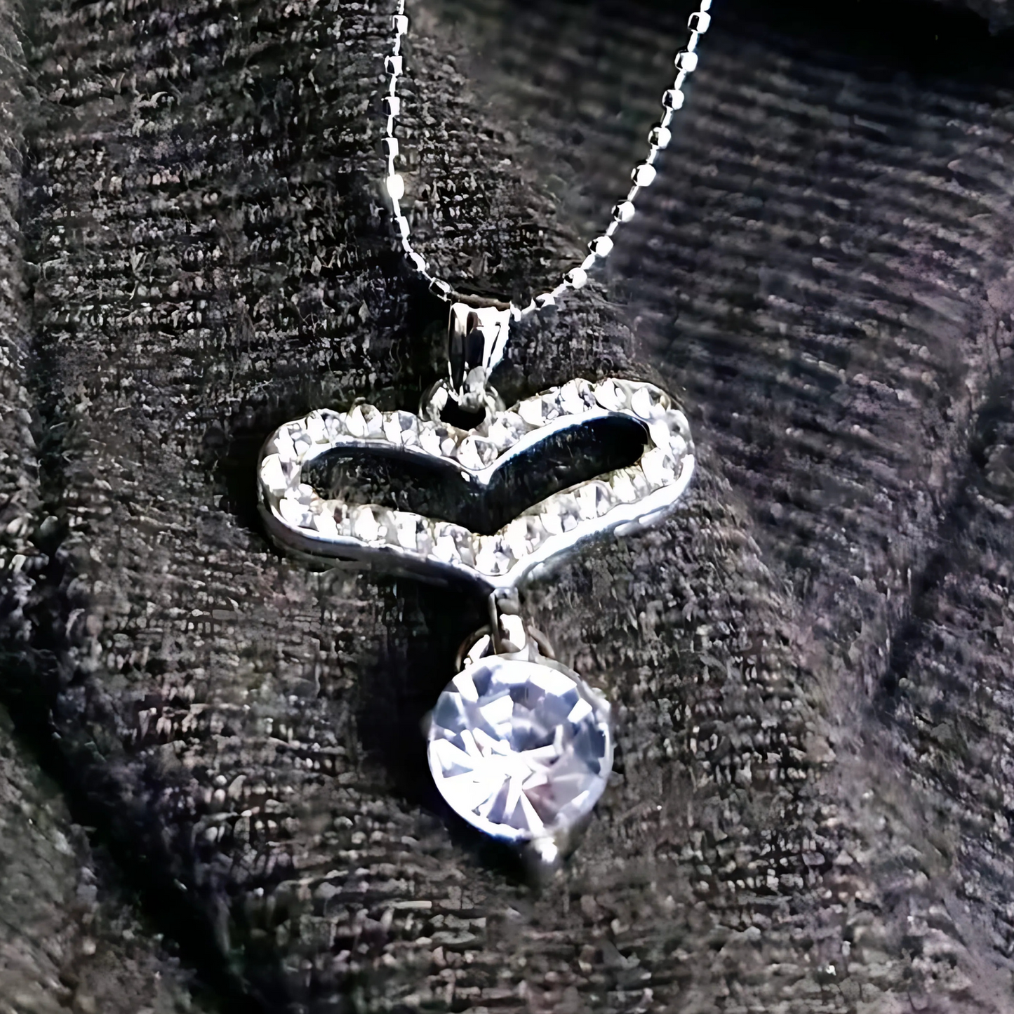 Heart-shaped necklace with a clear gemstone on a textured black background
