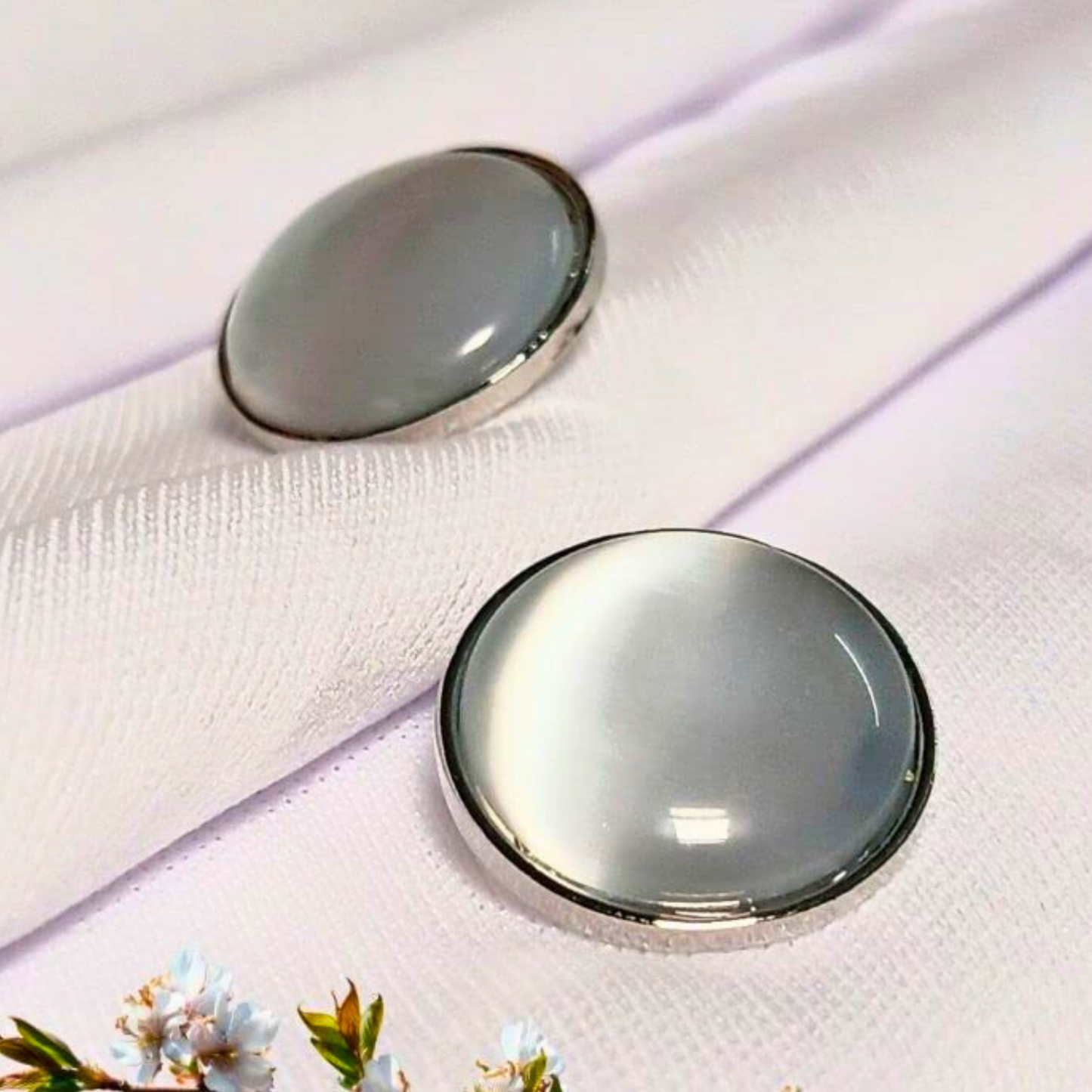 Two round, silver-framed glass objects on a white fabric background with floral elements.