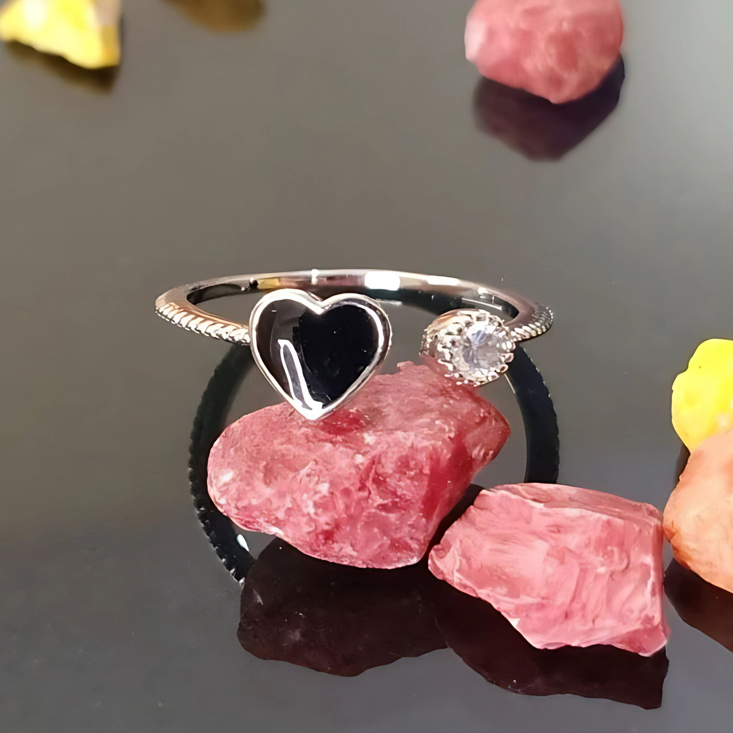 Silver ring with a heart-shaped gemstone on a dark surface with pink stones