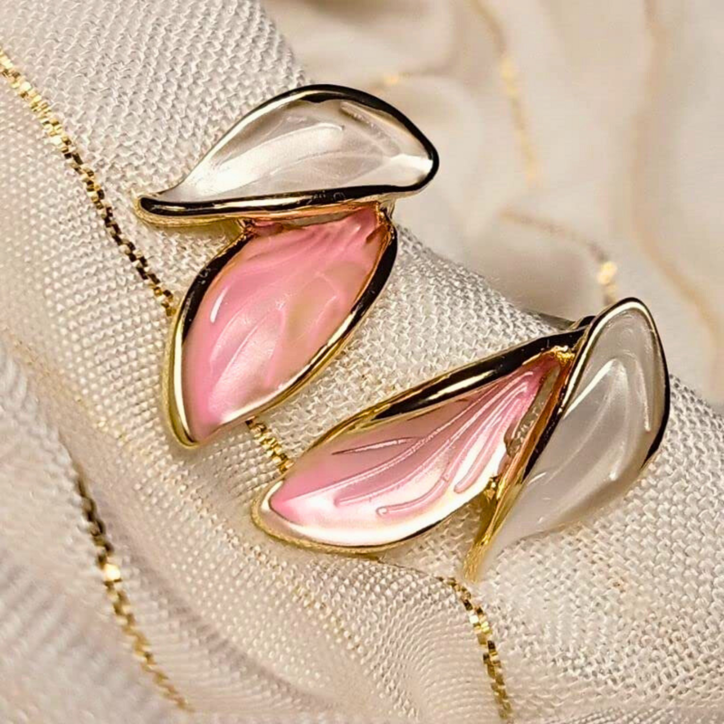 Pair of pink and gold earrings on a textured surface