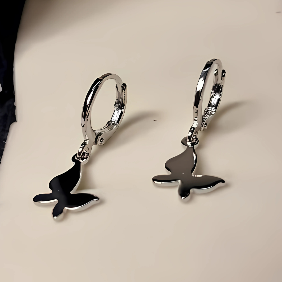 Silver earrings with whale tail designs on a beige background