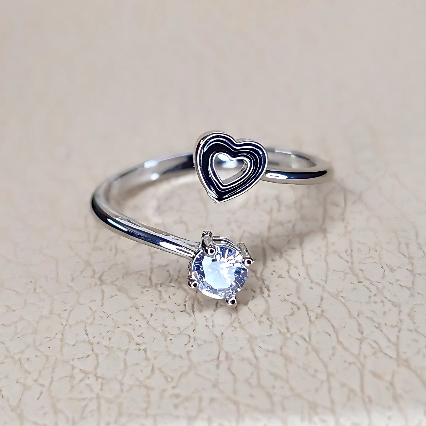 Silver ring with heart design and gemstone on a beige background