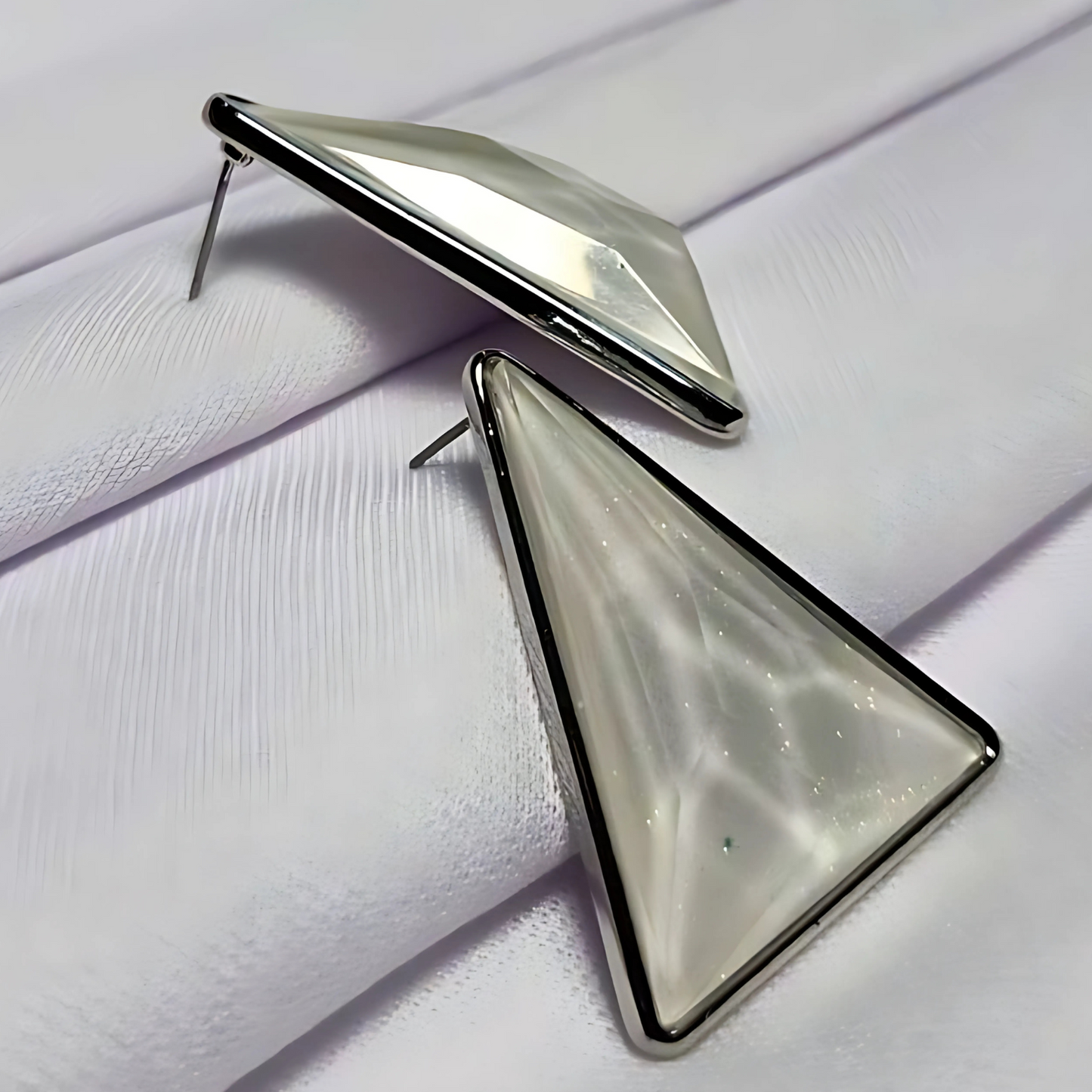 Triangular earrings with a metallic finish on a textured white surface