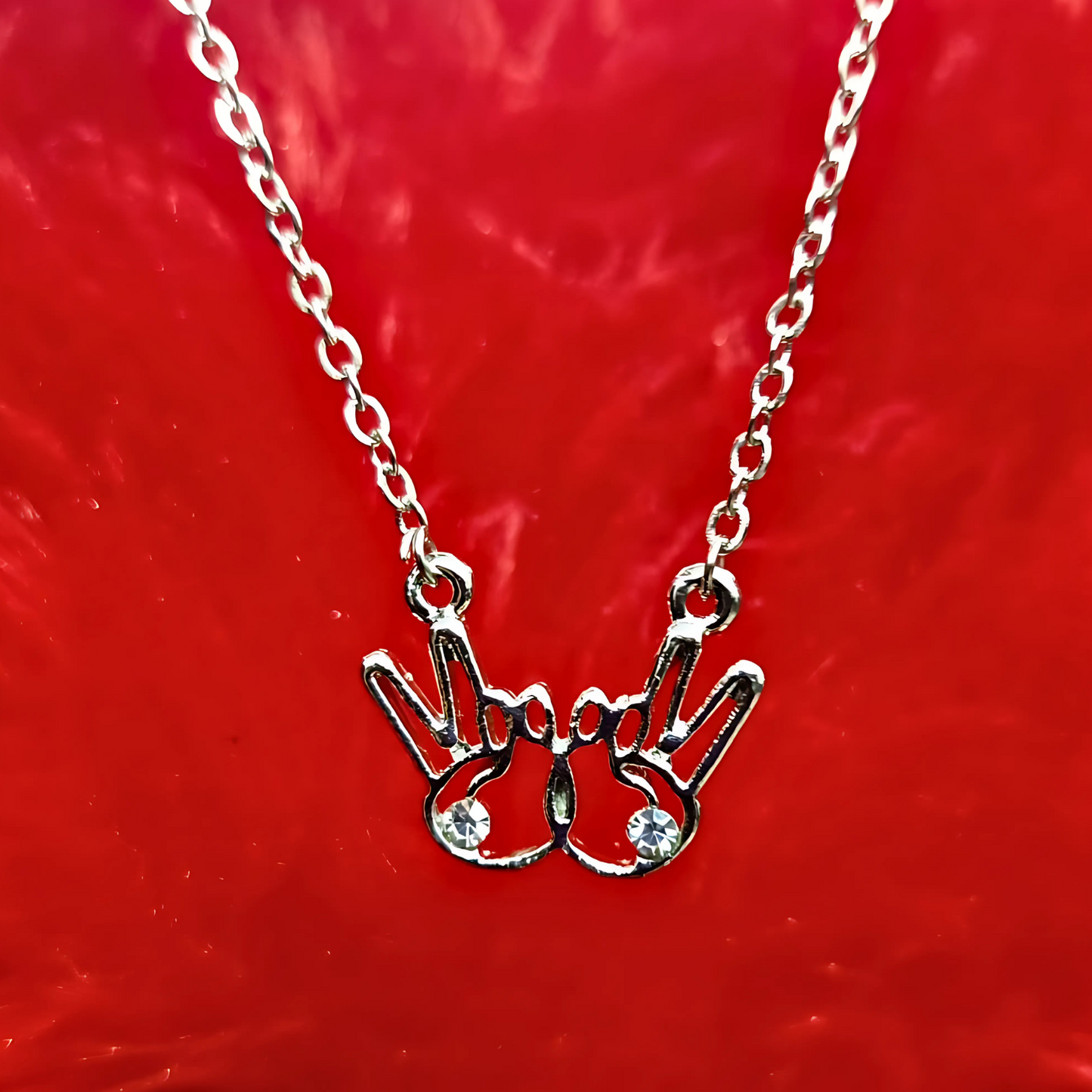 Silver necklace with a hand-shaped pendant on a red background