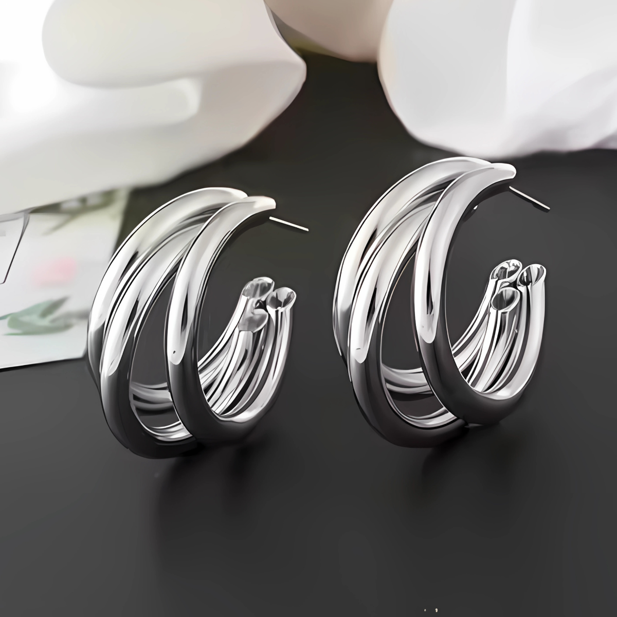 Silver hoop earrings on a dark surface with white flowers in the background