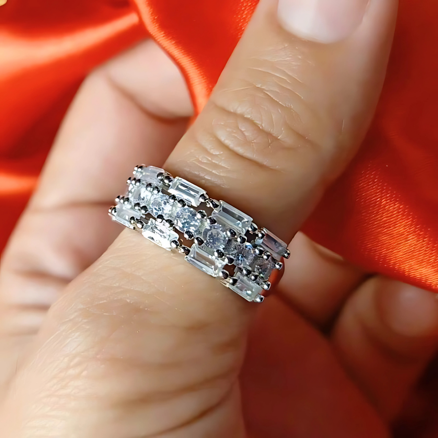 Close-up of a hand wearing a silver ring with multiple diamonds against a red fabric background