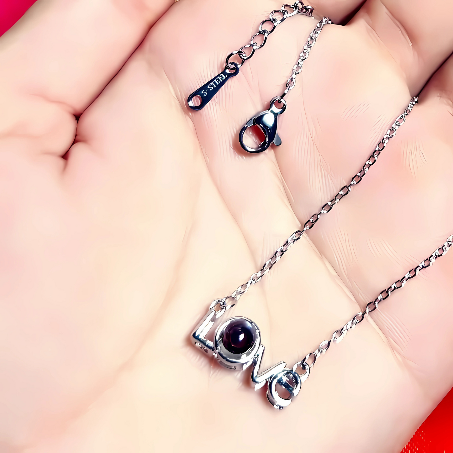 Silver necklace with 'LOVE' pendant on a hand against a pink background