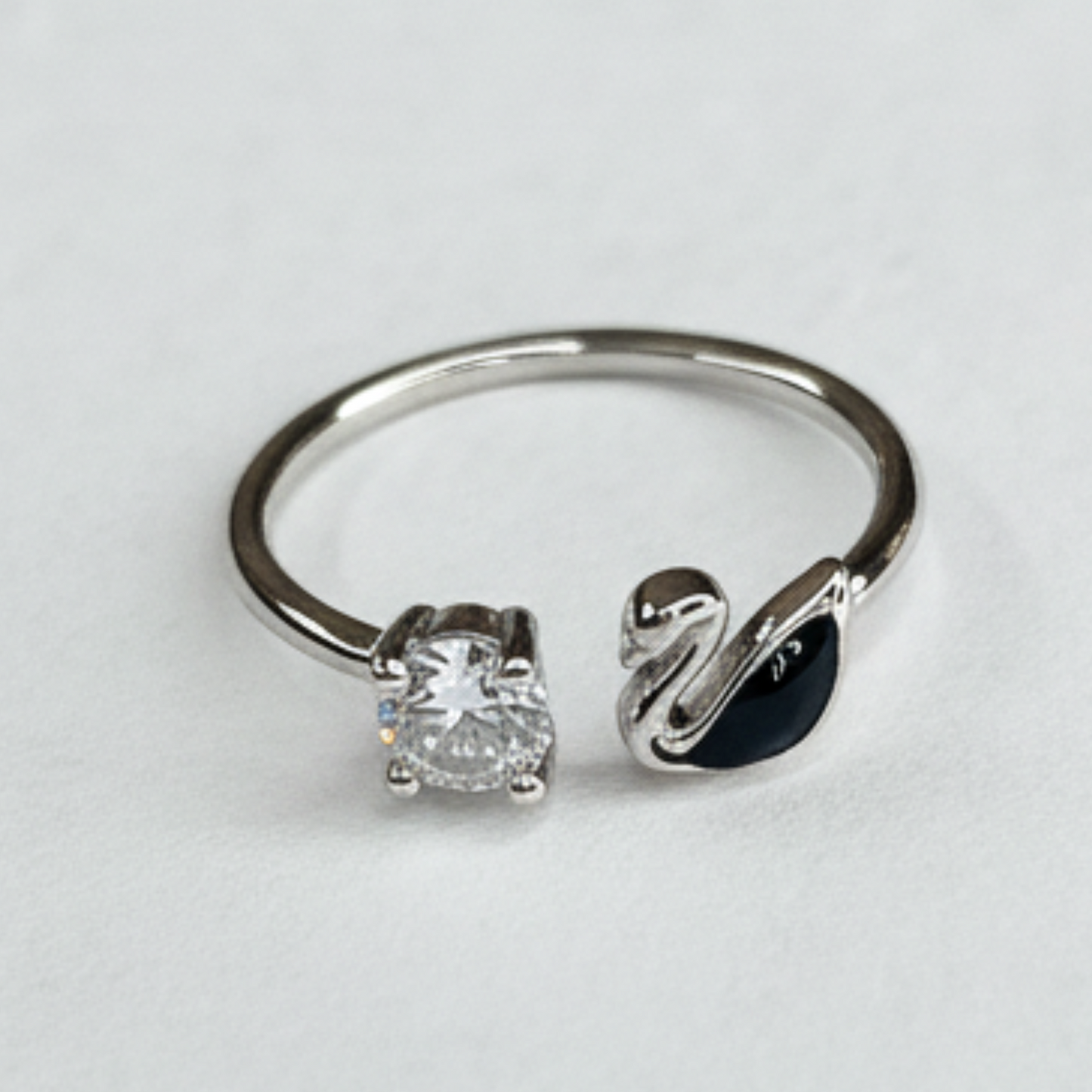 Silver ring with diamond and swan design on a light gray background