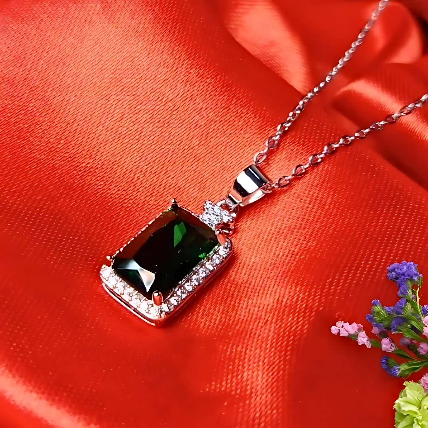 Silver necklace with a green gemstone pendant on a red fabric background