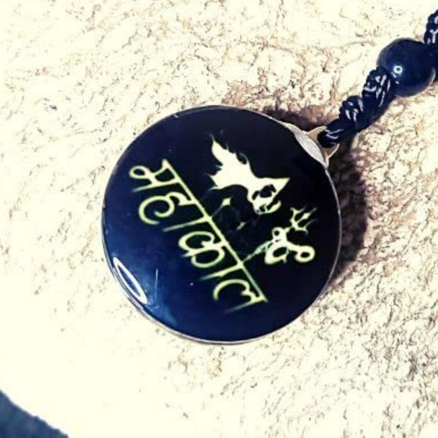Black pendant with gold text and design on a sandy background
