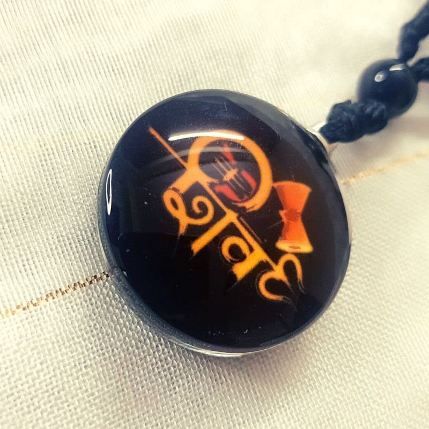 Black pendant with orange text on a white fabric background