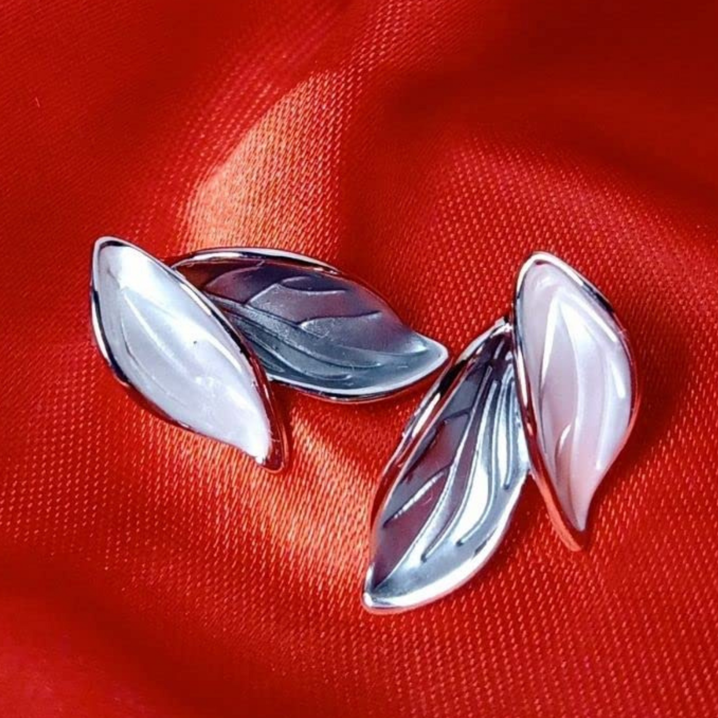 Silver leaf-shaped earrings on a red fabric background