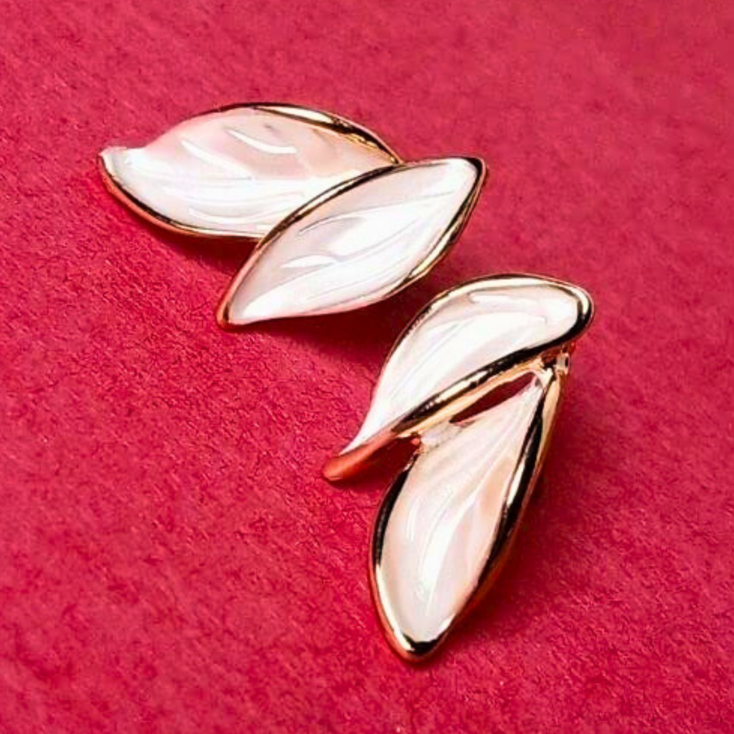 Pair of gold and white leaf-shaped earrings on a red background