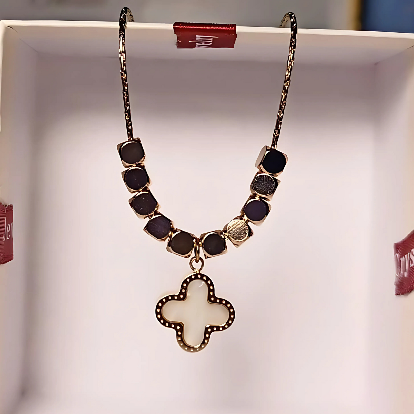 Necklace with gold beads and a clover-shaped pendant on a white background