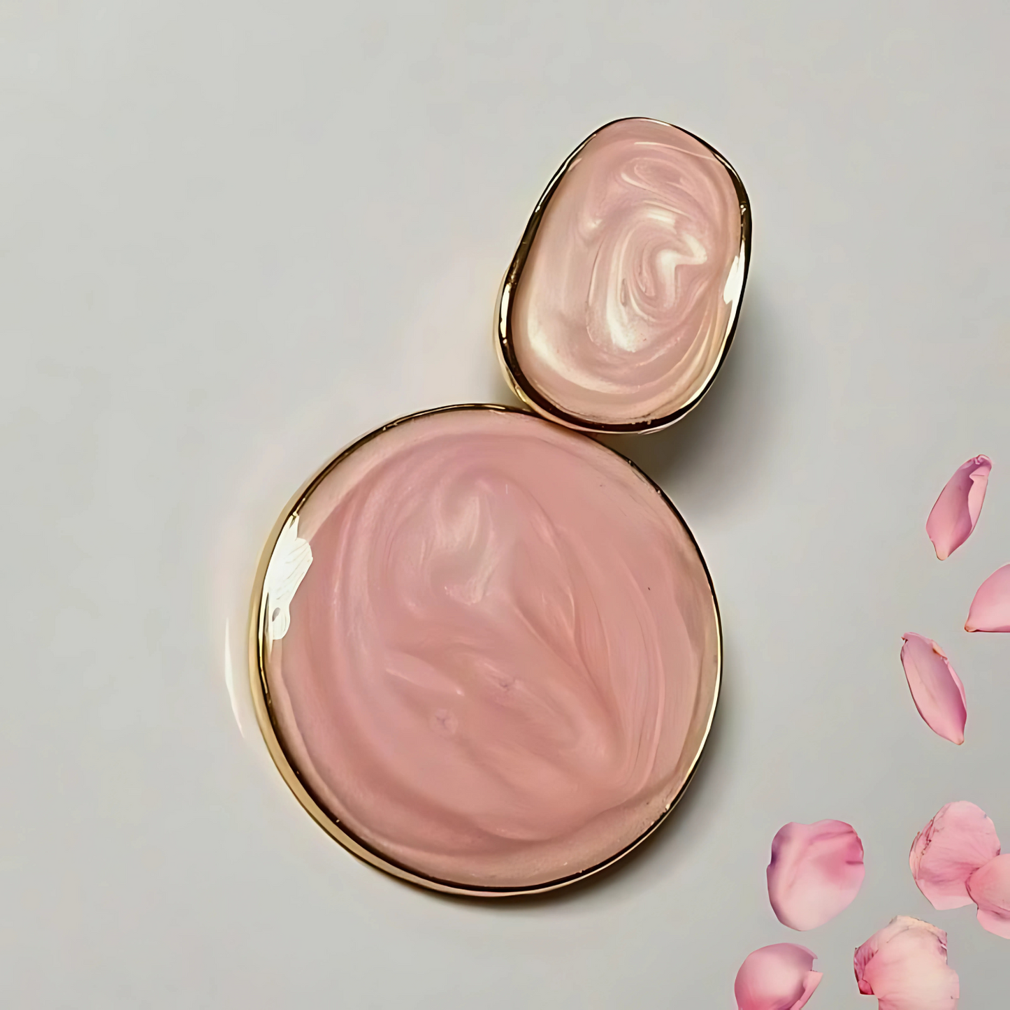 Pink earrings with gold accents on a light gray background with pink petals.
