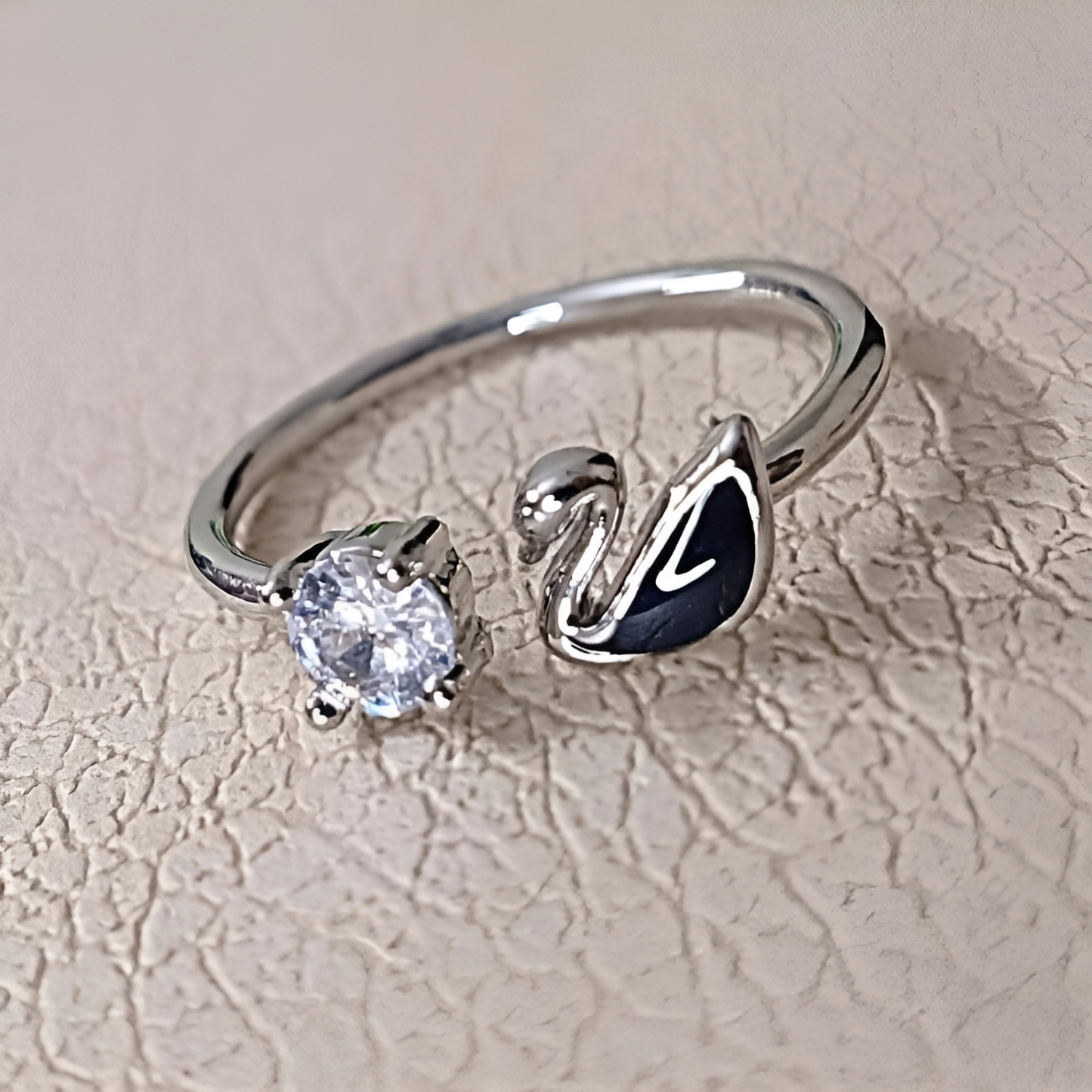 Silver ring with a diamond and black gemstone on a textured beige background