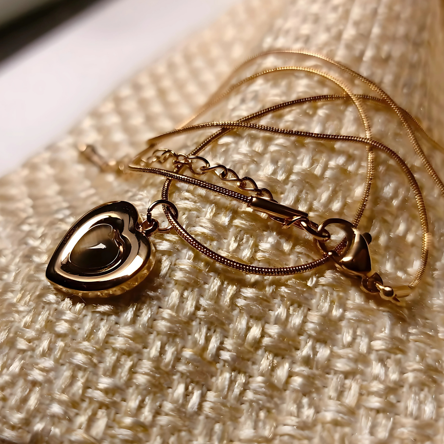 Gold necklace with a heart-shaped pendant on a textured beige surface
