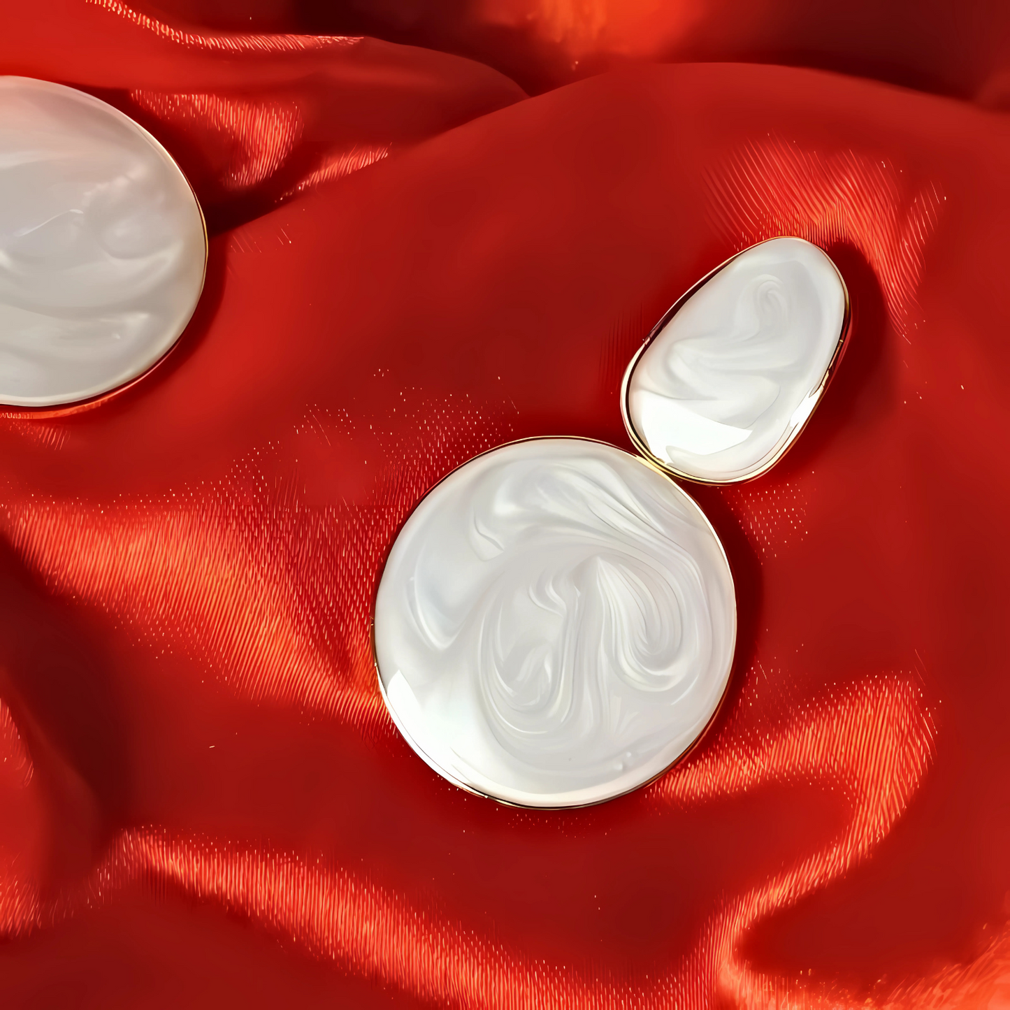 Two white marbled round objects with gold edges on a red fabric background