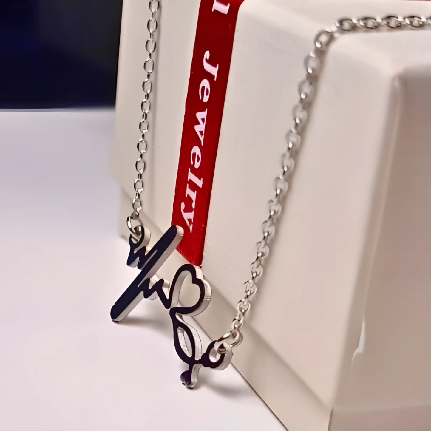 Silver necklace with a heart-shaped pendant on a white stand with a red ribbon label.