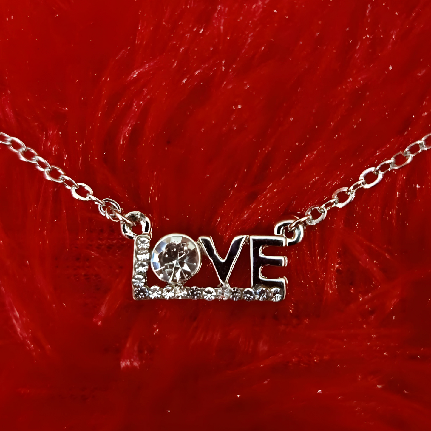 Silver 'LOVE' necklace with a small round pendant on a red furry background