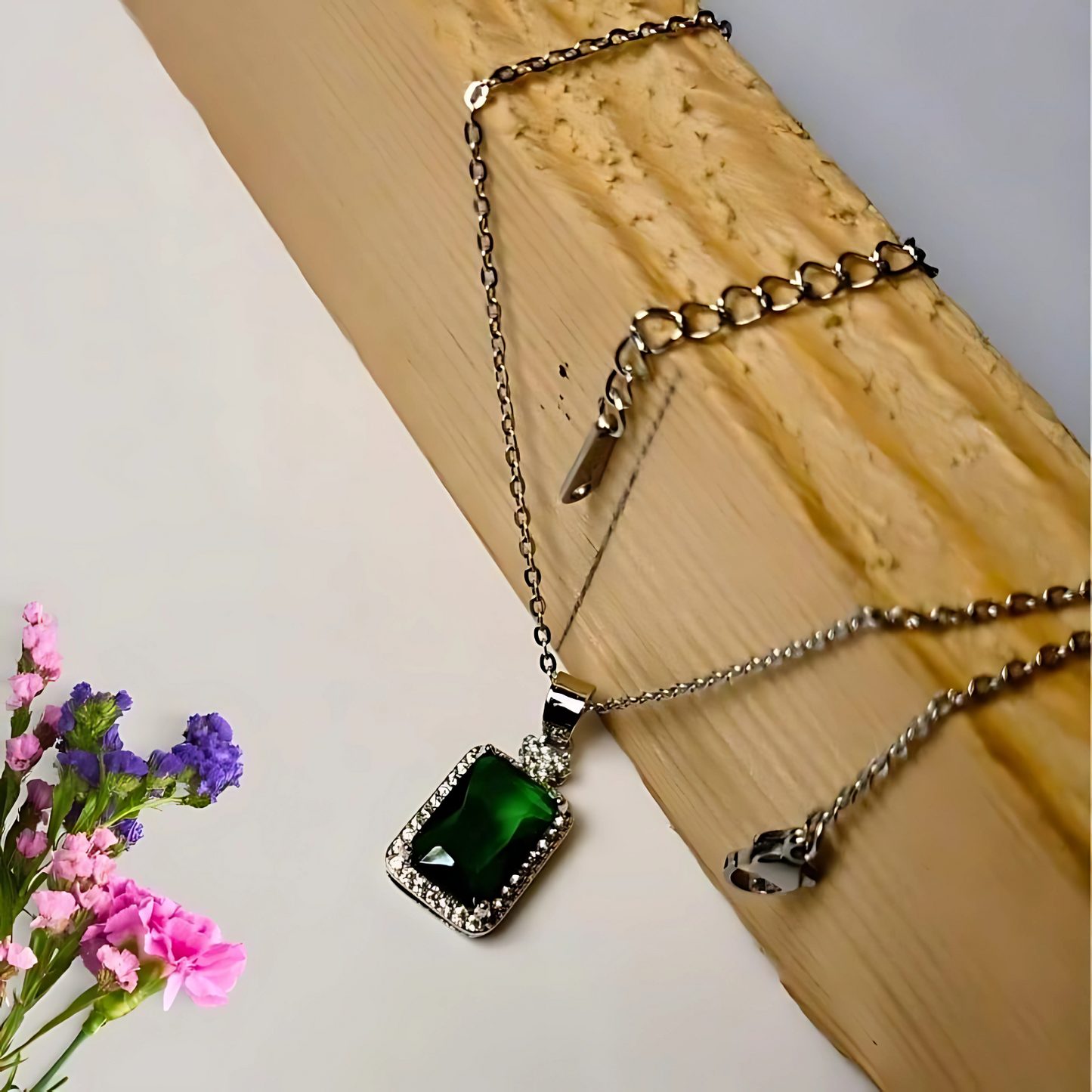 Necklace with a green pendant on a wooden surface with flowers