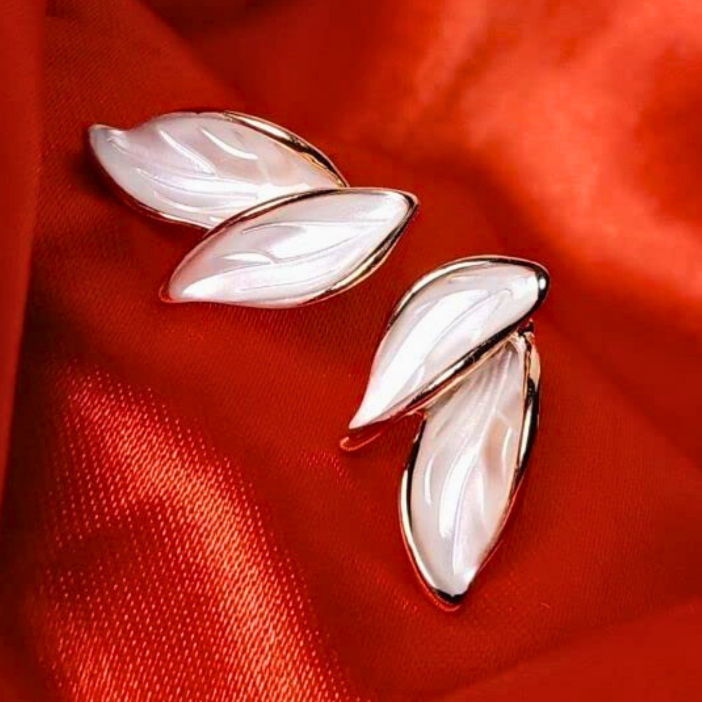Pair of leaf-shaped earrings on a red fabric background