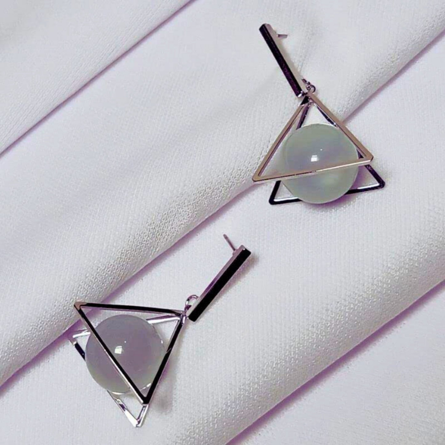 Geometric earrings with triangular design on a white fabric background