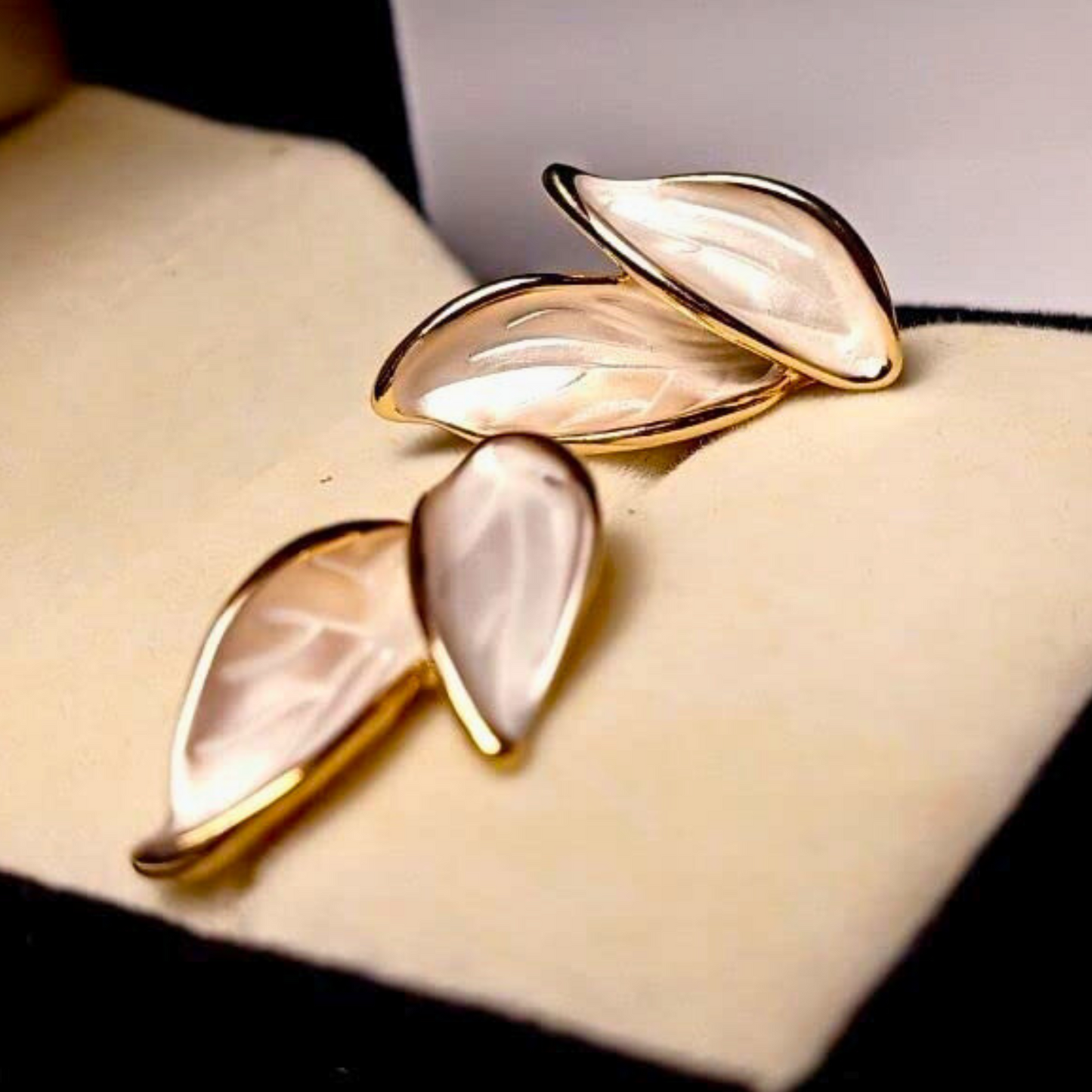 Pair of gold and white earrings on a beige cushion