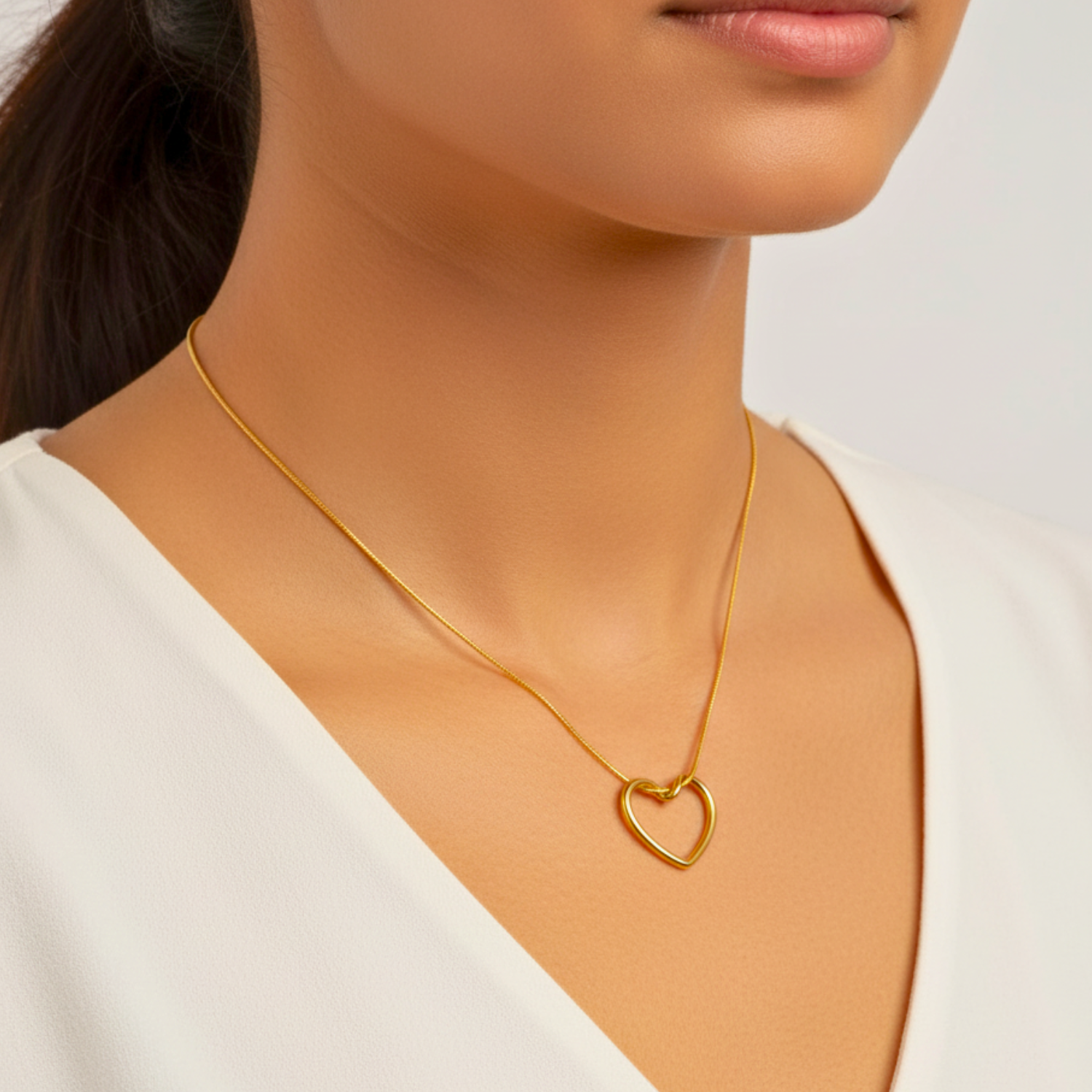 Gold necklace with a heart pendant worn by a person against a neutral background