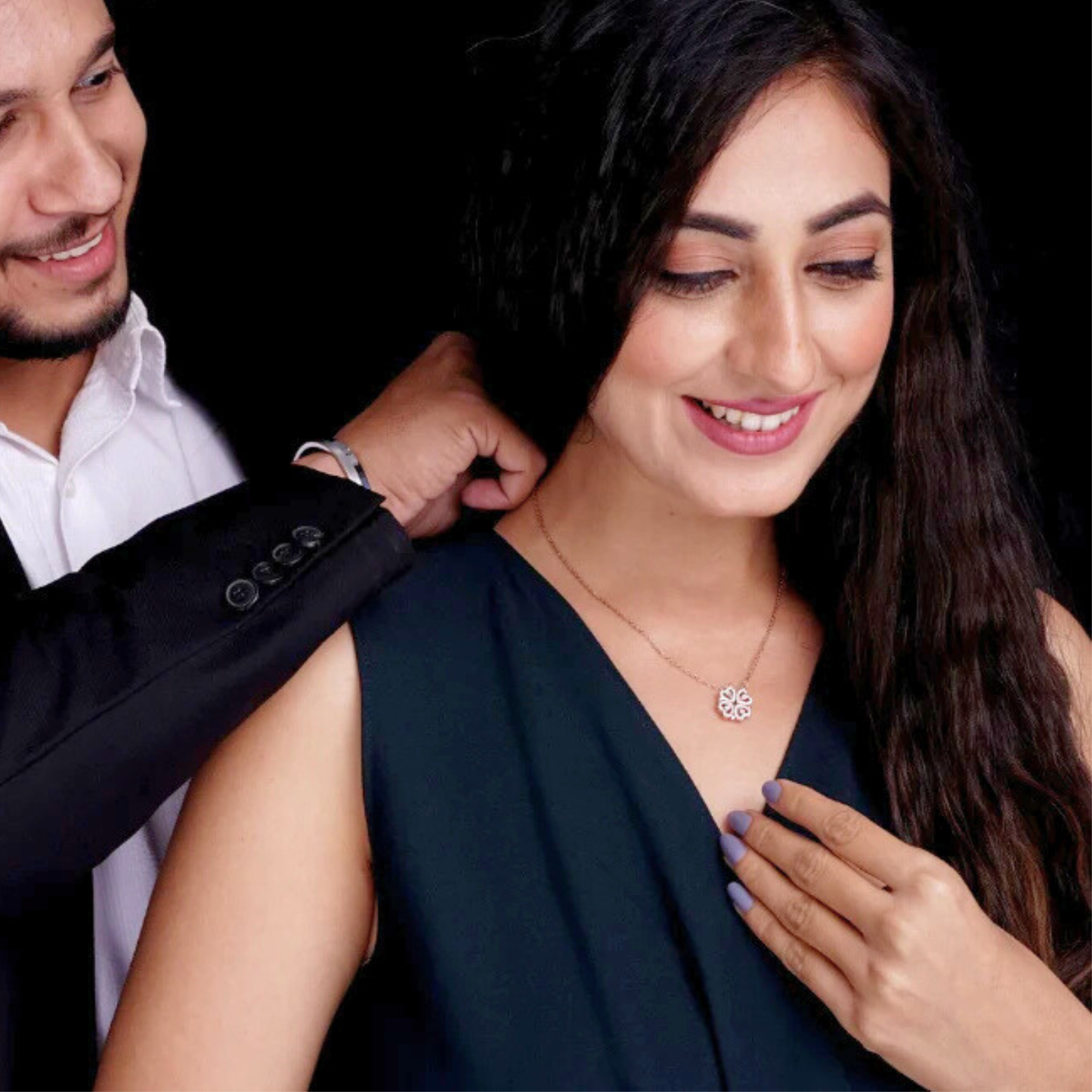 Woman wearing a necklace with a man adjusting it against a black background