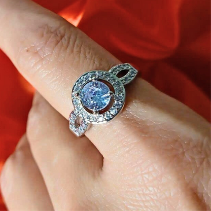 Silver ring with a blue gemstone on a finger against a red background