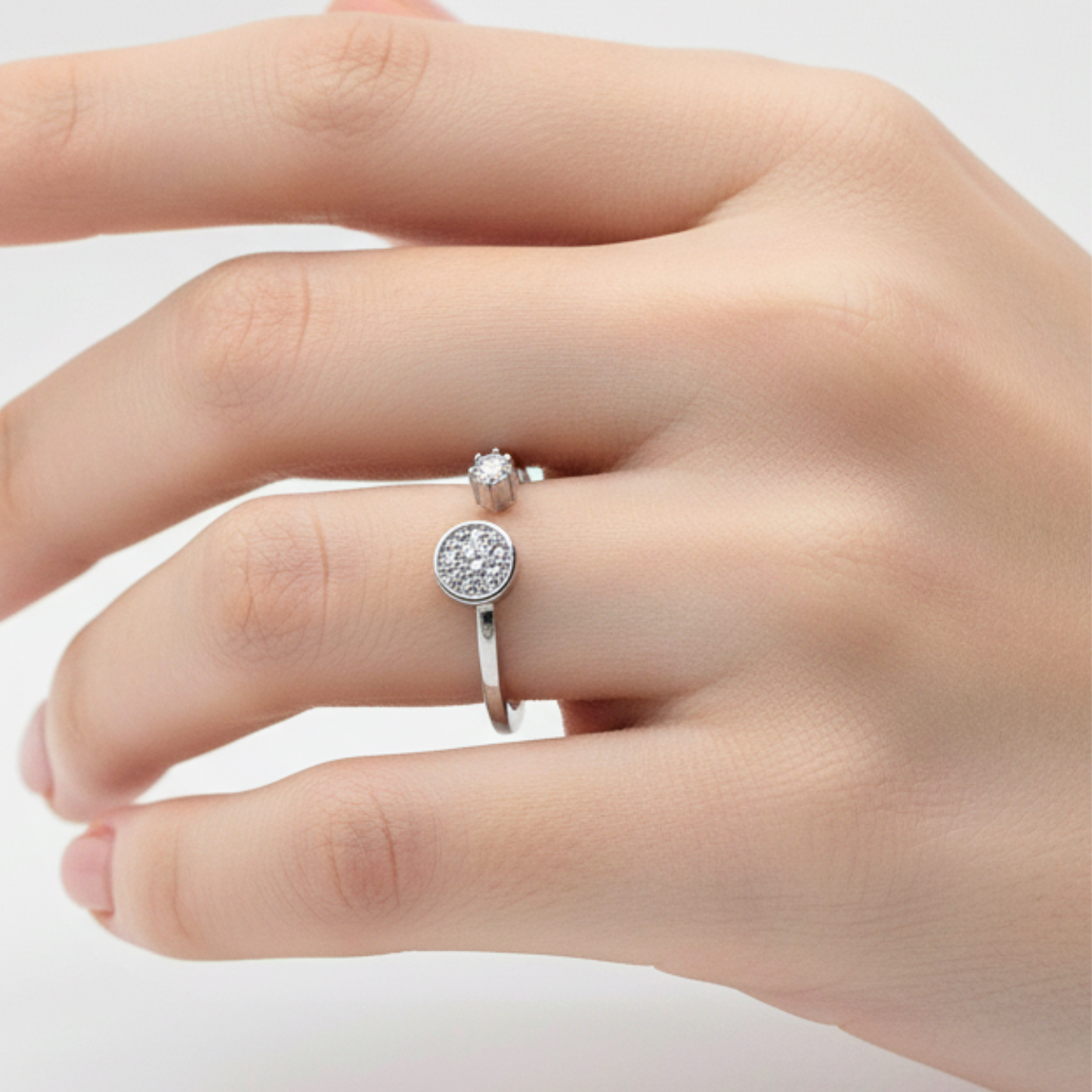 Silver ring with a circular design on a person's finger against a light background