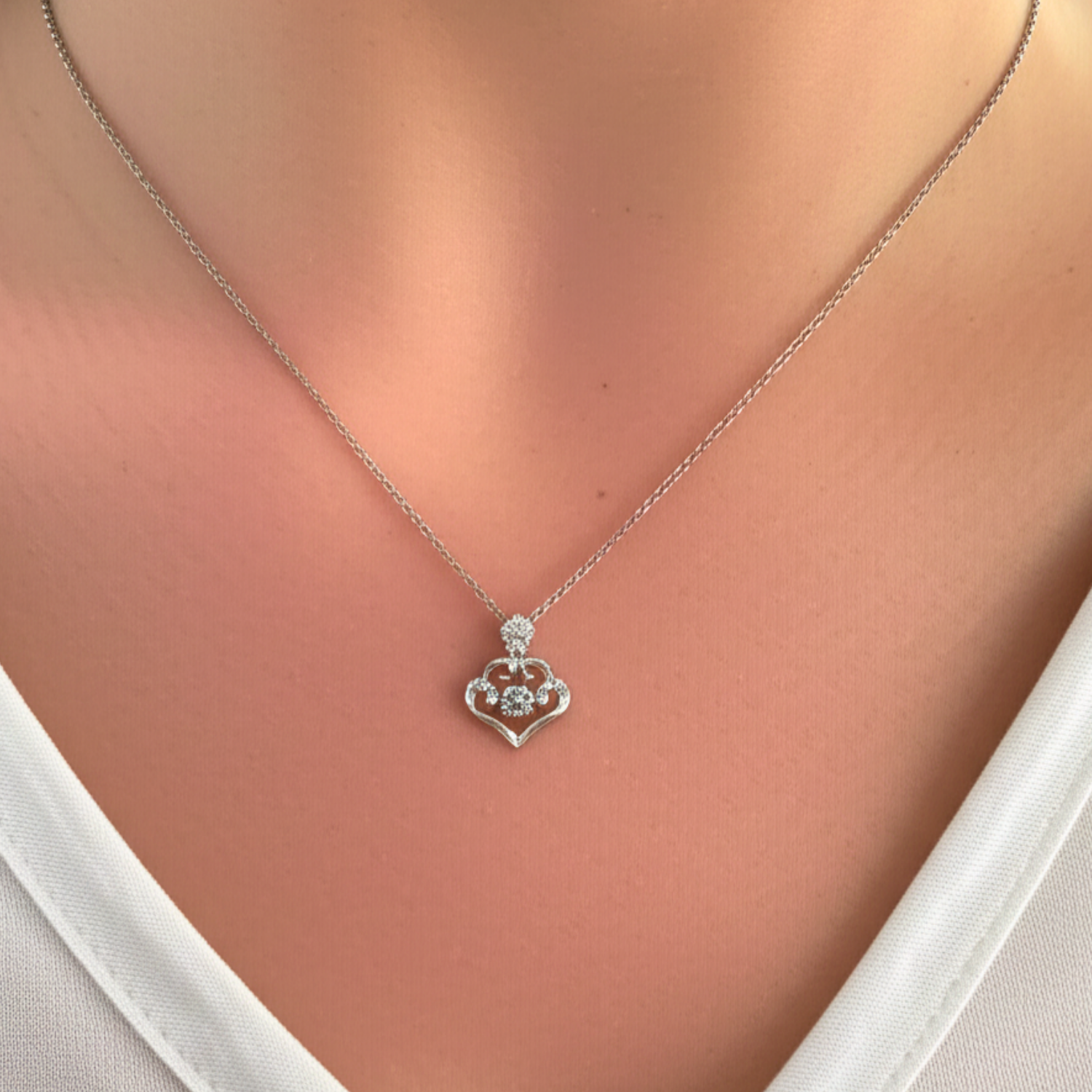 Silver necklace with a claddagh pendant on a person wearing a white top.