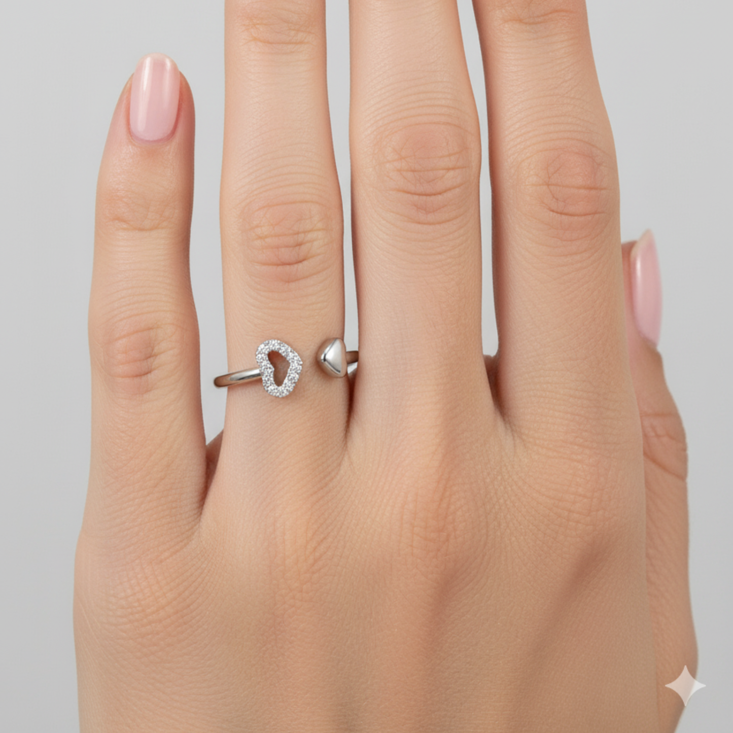 Silver ring with heart design on a hand against a gray background