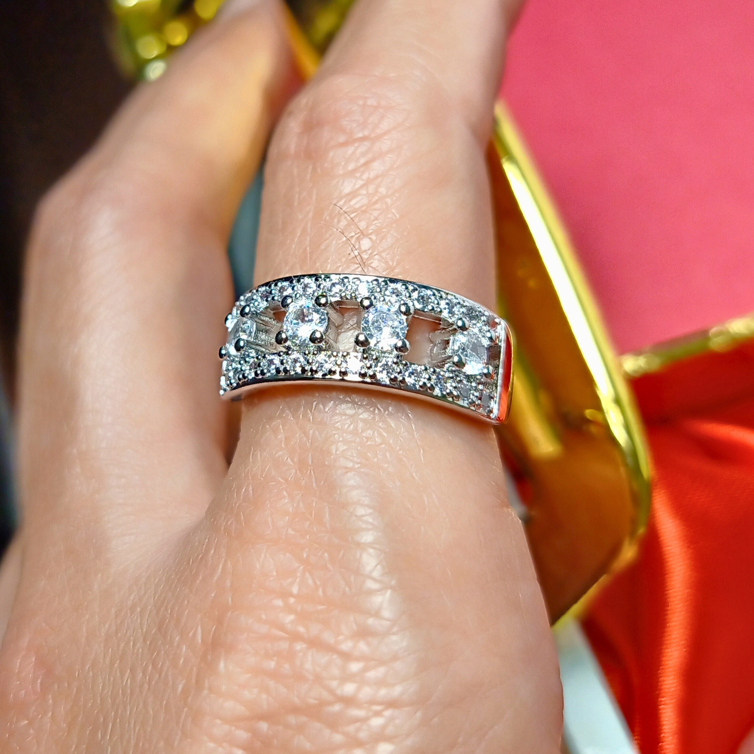 Silver ring with diamonds on a finger against a red and gold background