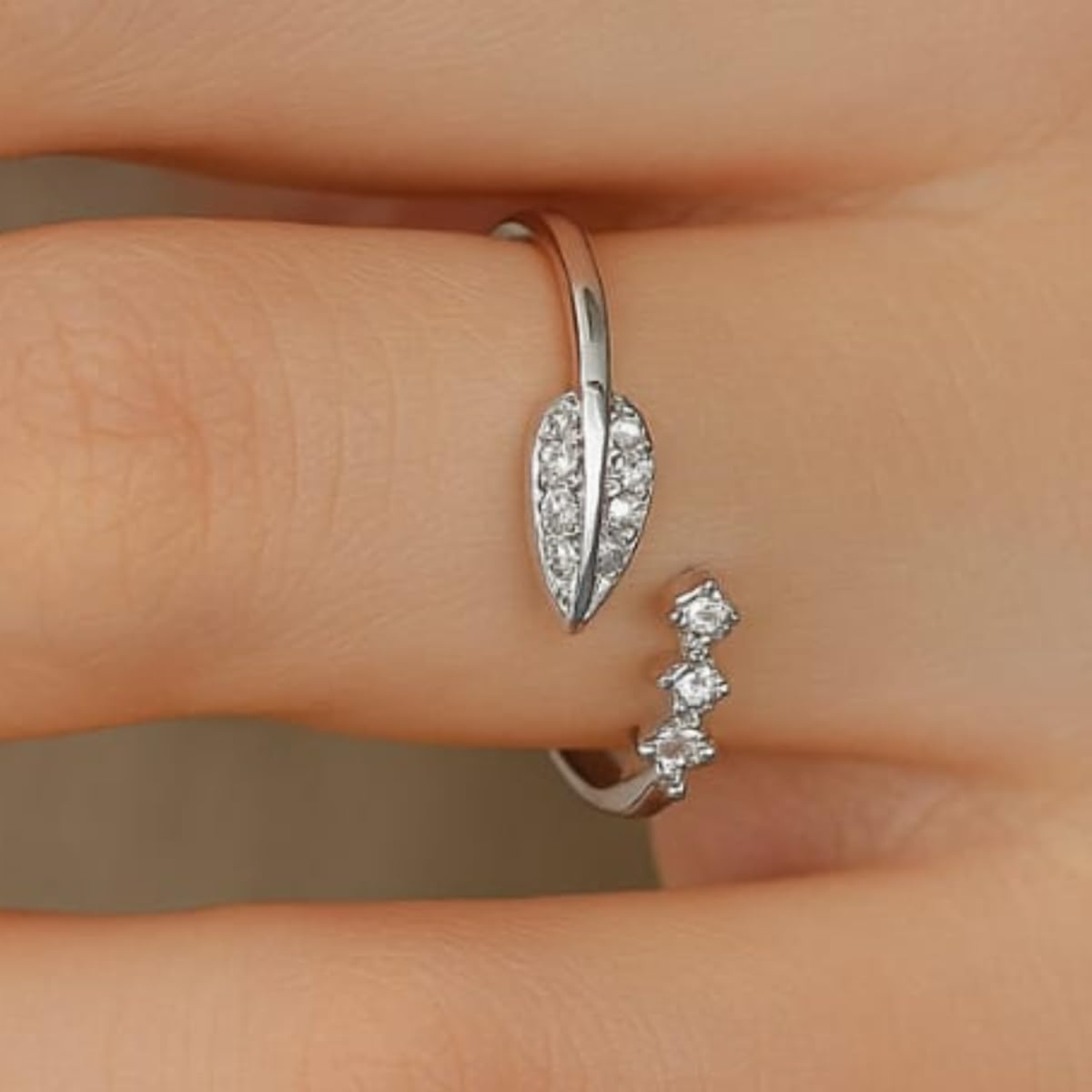Silver leaf-shaped earring on a finger against a neutral background