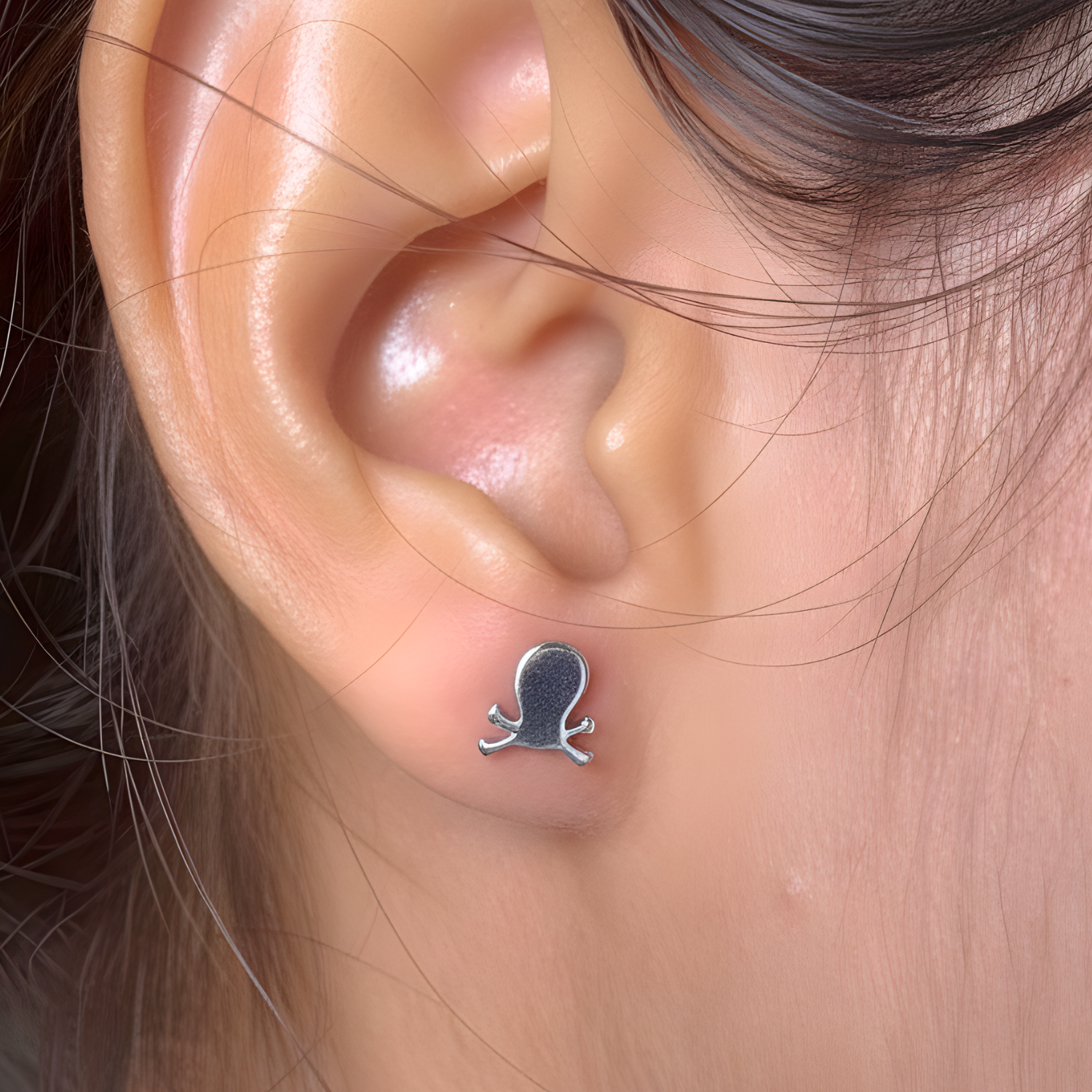 Silver octopus earring worn on a person's ear