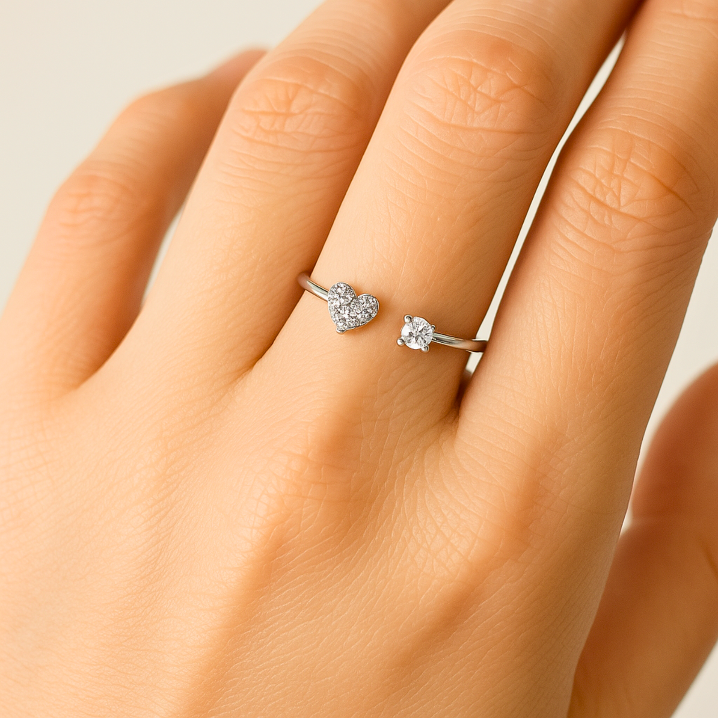 Silver ring with a heart-shaped diamond on a hand against a neutral background