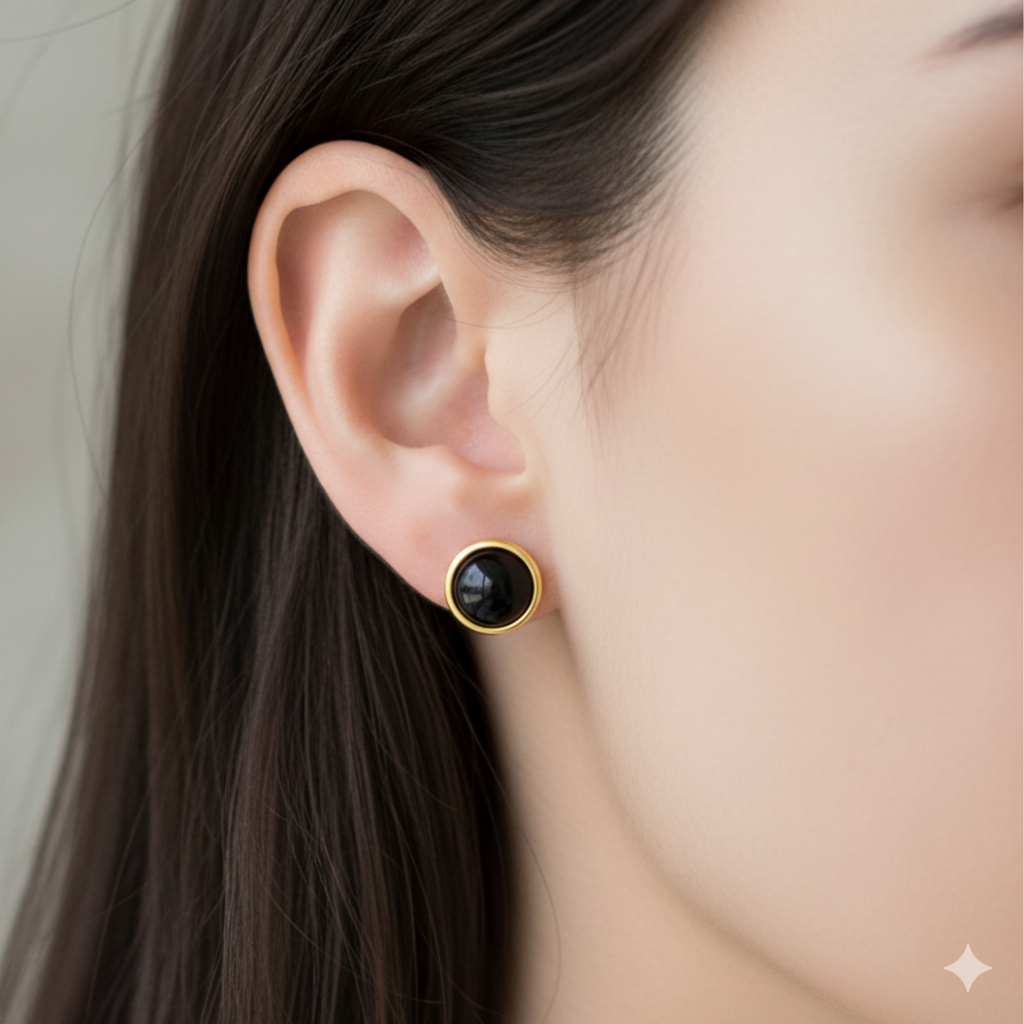 Close-up of an ear wearing a black stud earring with gold setting.