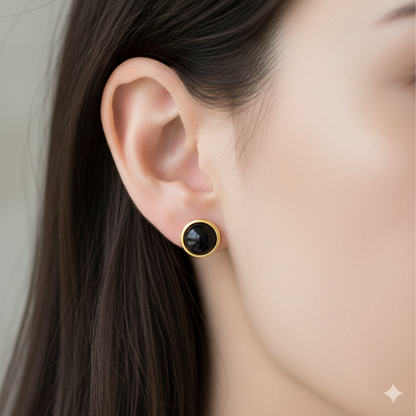 Close-up of an ear wearing a black stud earring with gold setting.