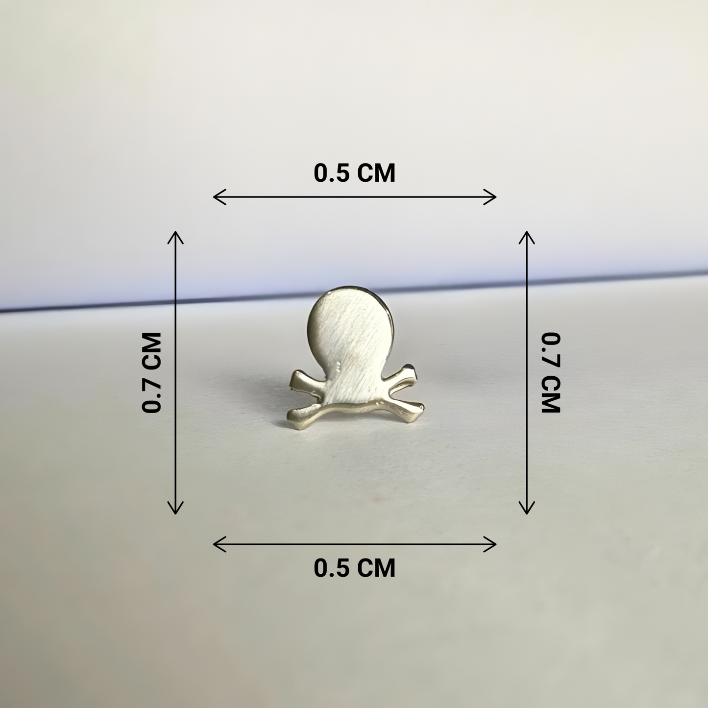 Silver skull and crossbones earring with dimensions on a light gray background